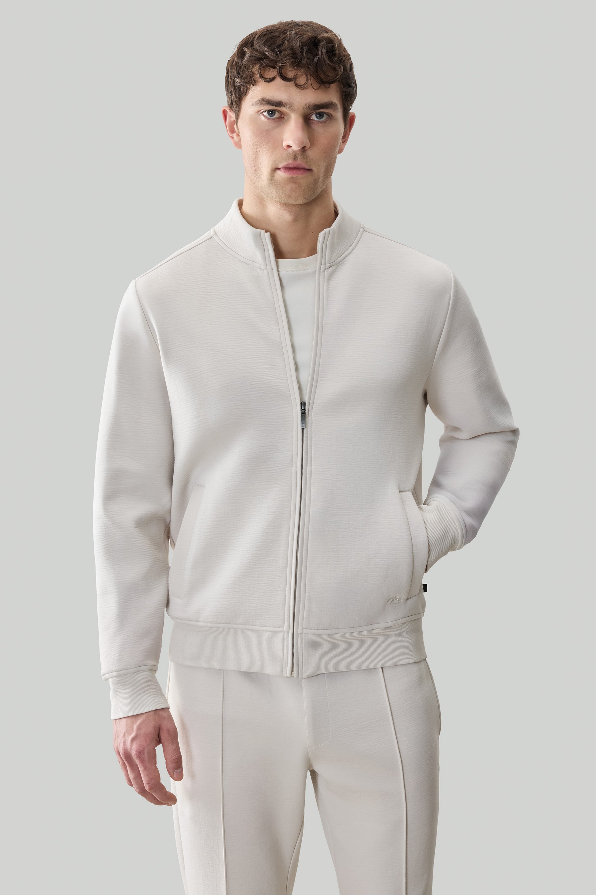 Man wearing cream-colored long sleeve full-zip jacket with ribbed texture and matching pants.