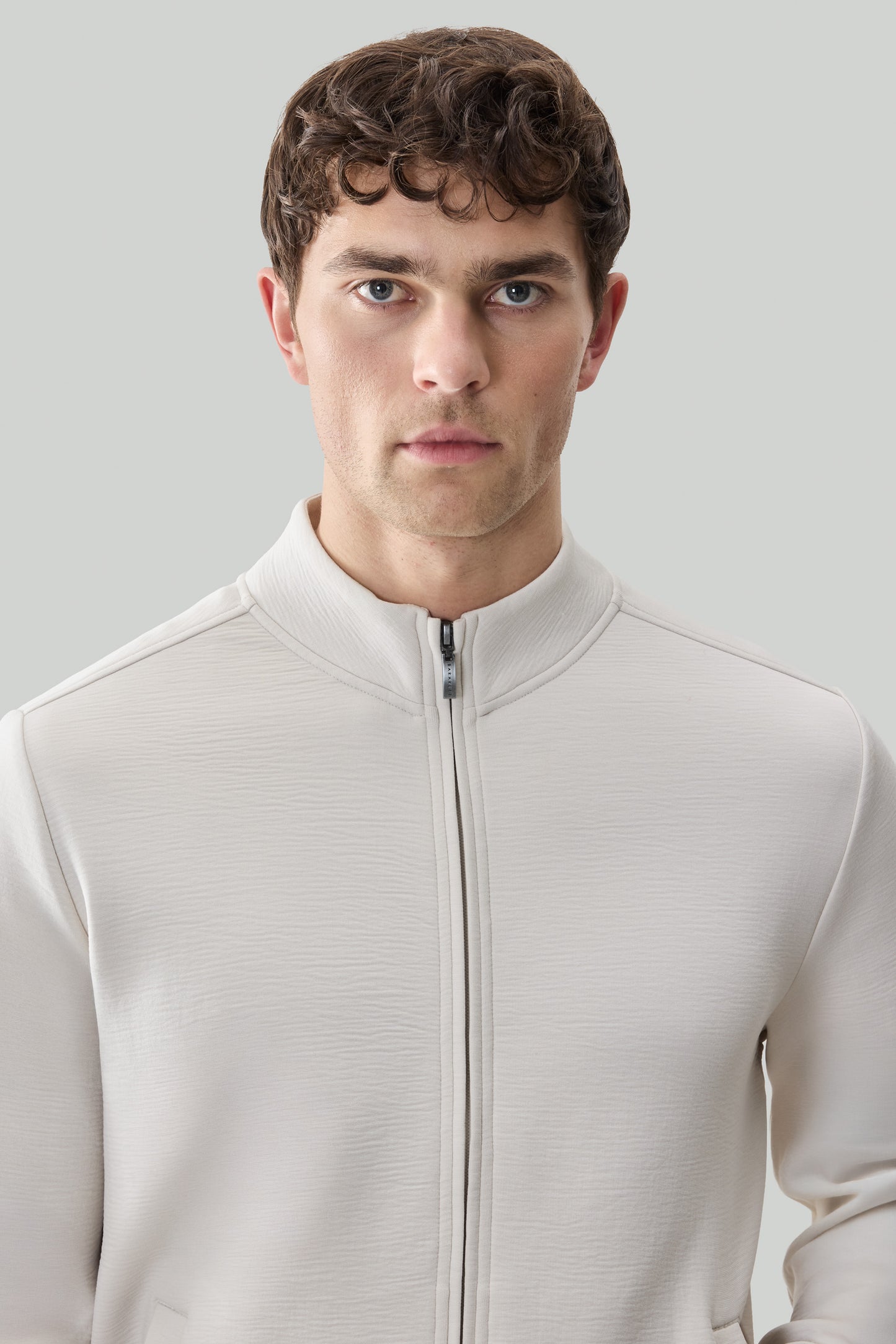Man wearing cream-colored long sleeve full zip jacket with textured fabric and mock neck collar.
