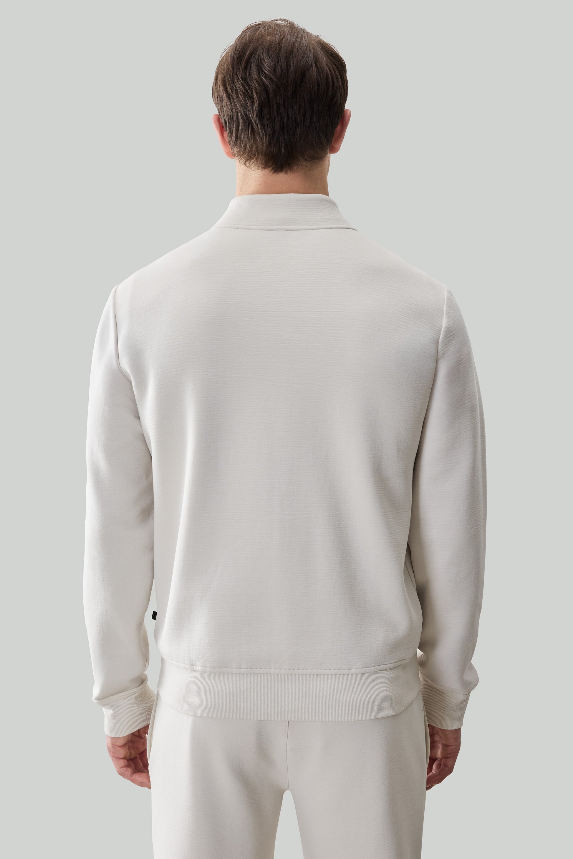 Man wearing cream-colored long sleeve full zip jacket with ribbed collar and cuffs, shown from back.