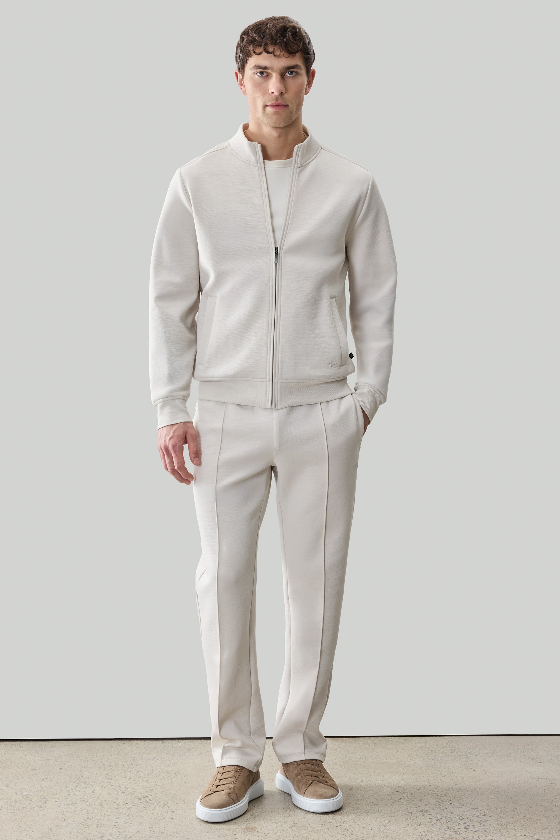 Man wearing cream-colored long sleeve full zip jacket and matching pants with tan sneakers.