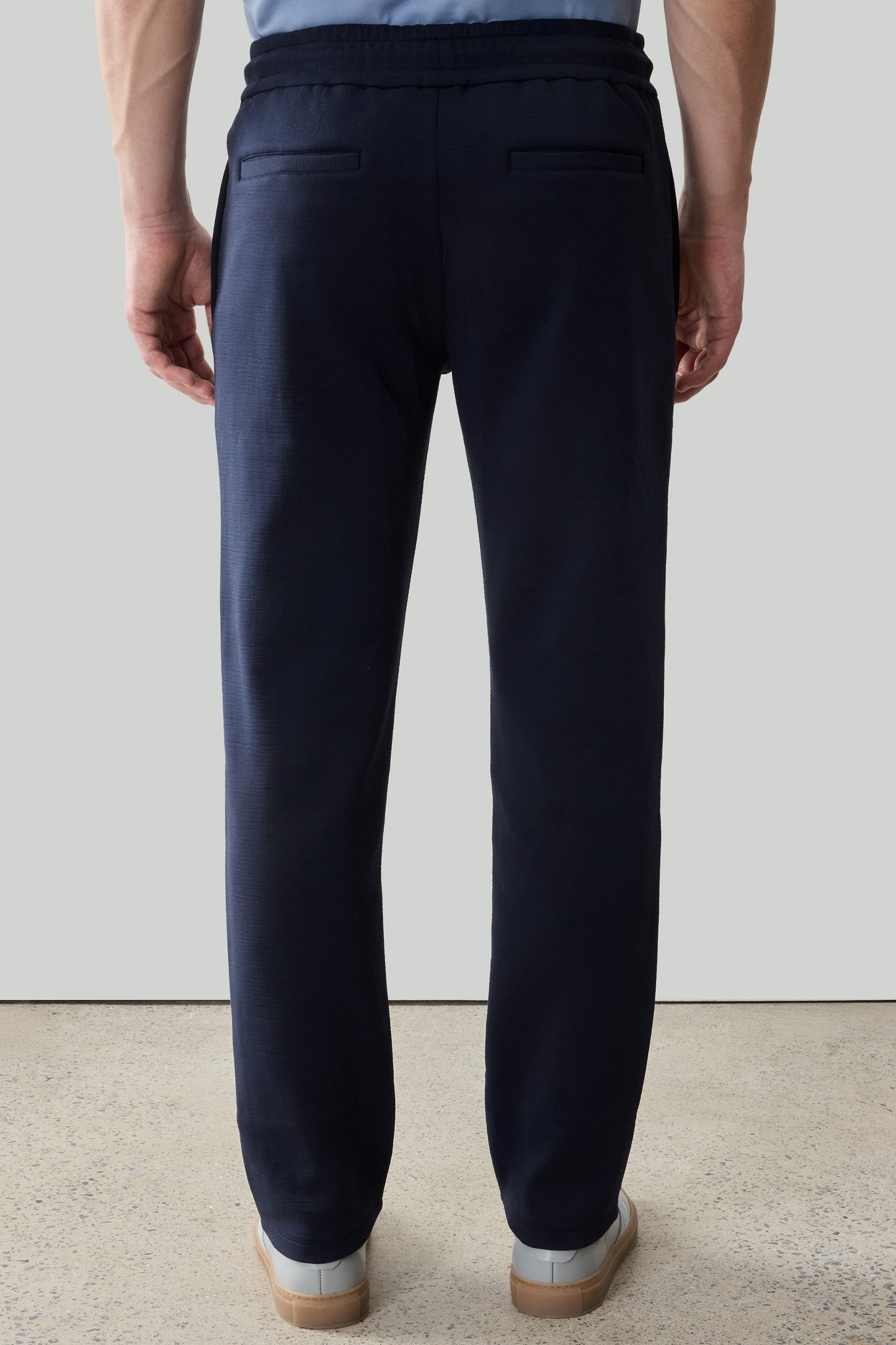 Man wearing navy jogger pants with drawstring waist and rear pockets, shown from back view.