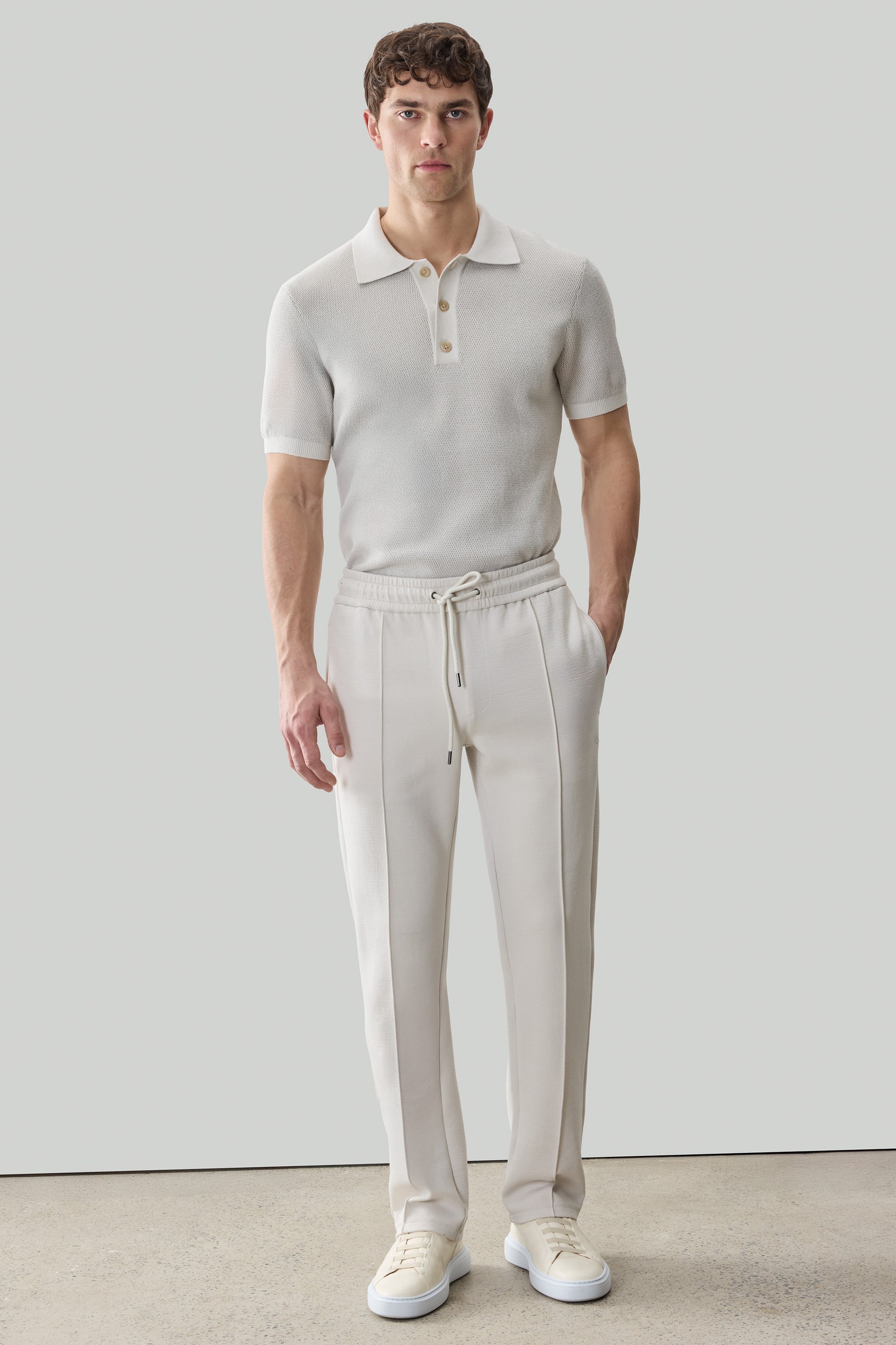 Man wearing beige Kenji jogger pants with drawstring waist and white polo shirt.