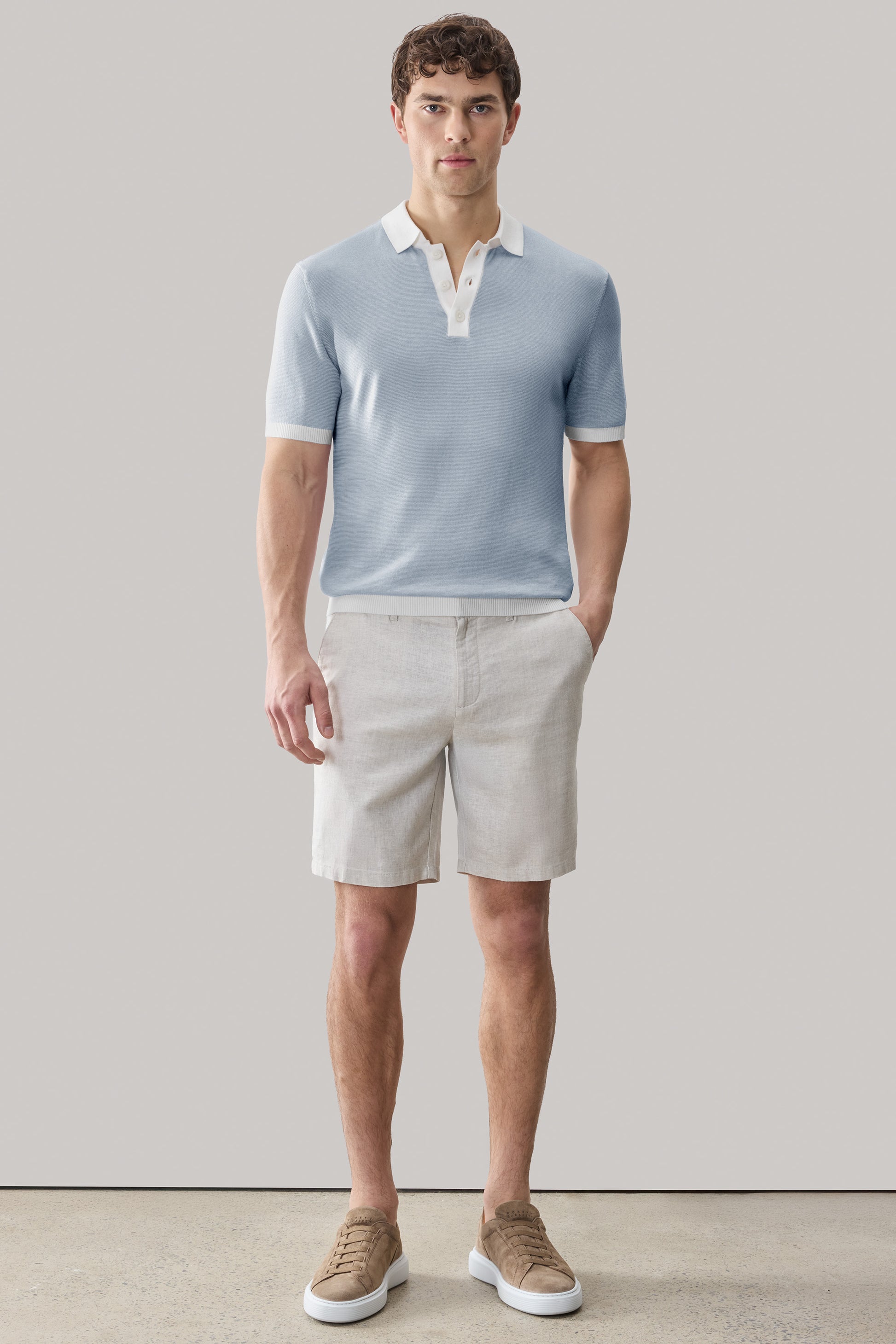 Man wearing light blue sweater polo with white collar and cream shorts.