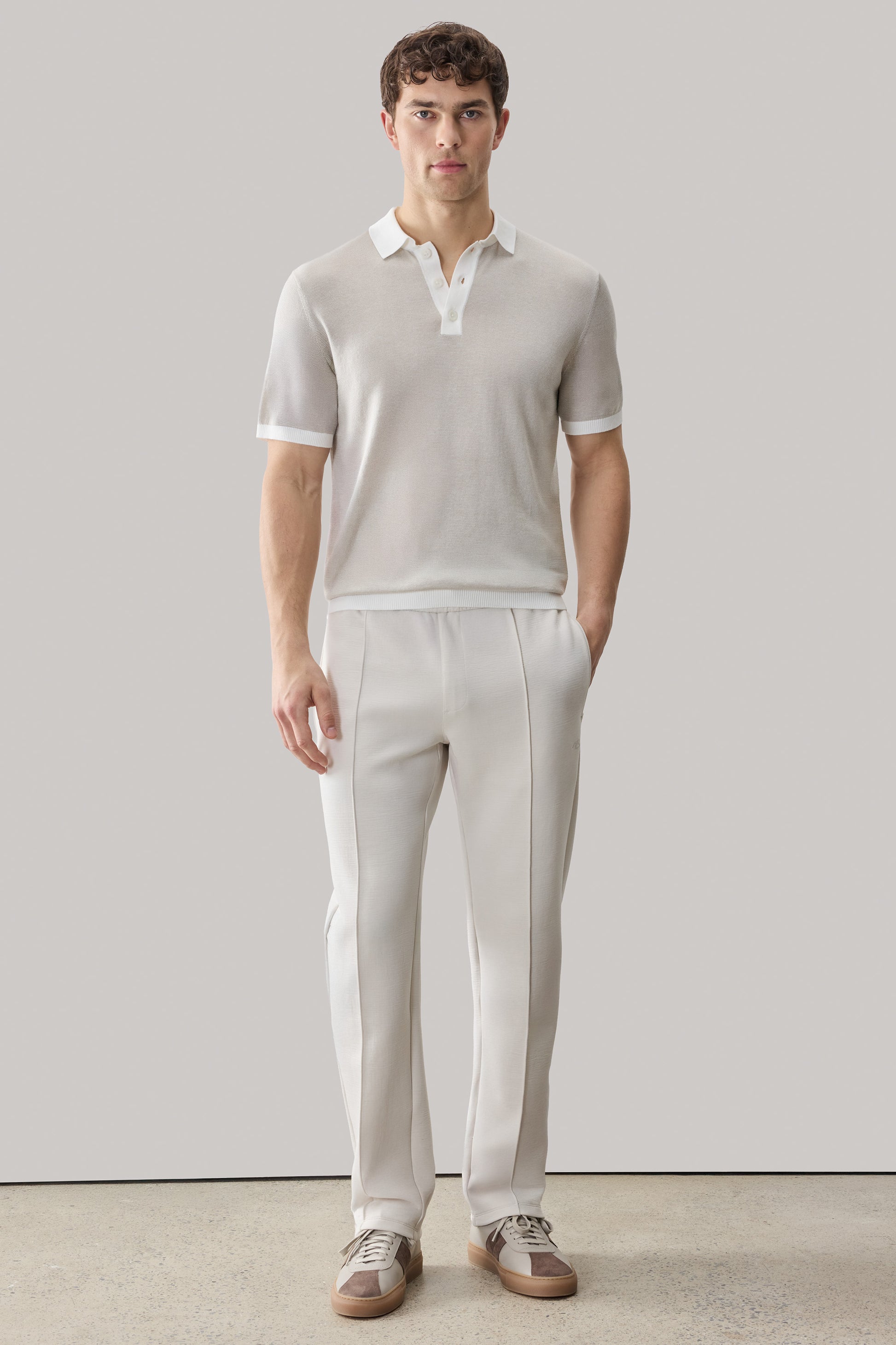 Man wearing cream polo shirt with white collar and trim, paired with cream trousers and two-tone sneakers.