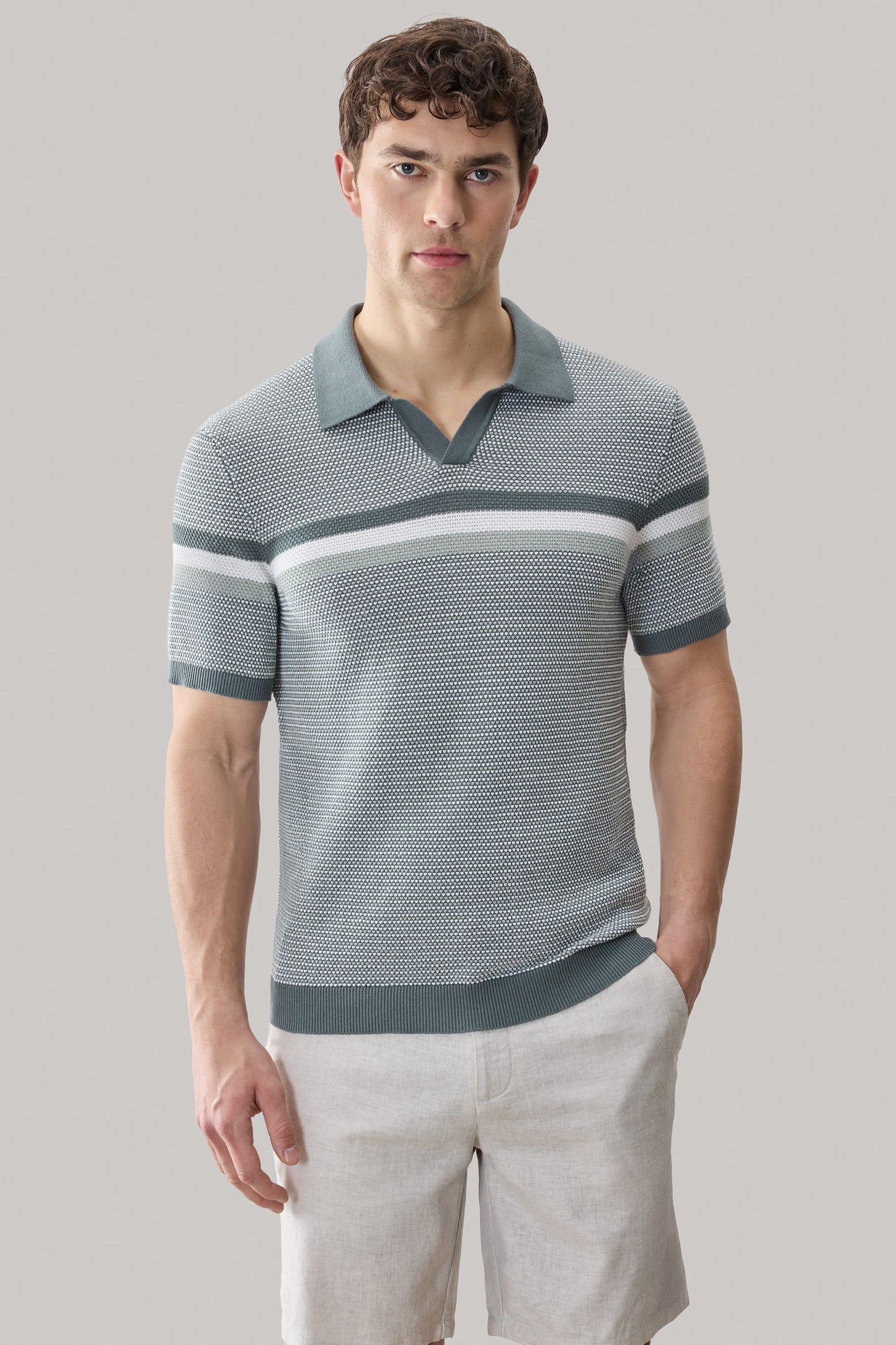 Man wearing gray and white striped short-sleeve polo sweater with open collar and light tan shorts.