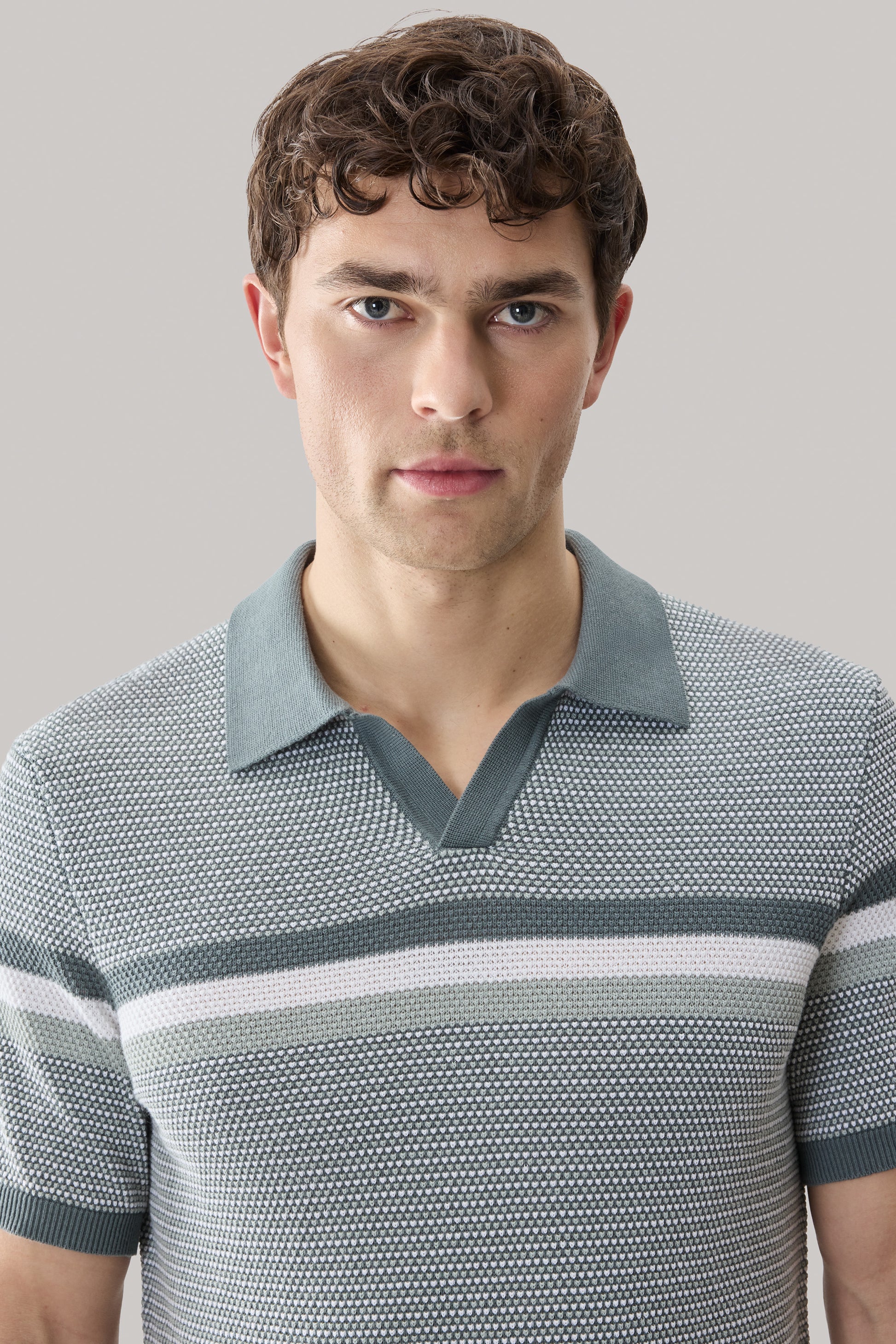 Man wearing gray and white striped open collar sweater polo with textured knit fabric and short sleeves.