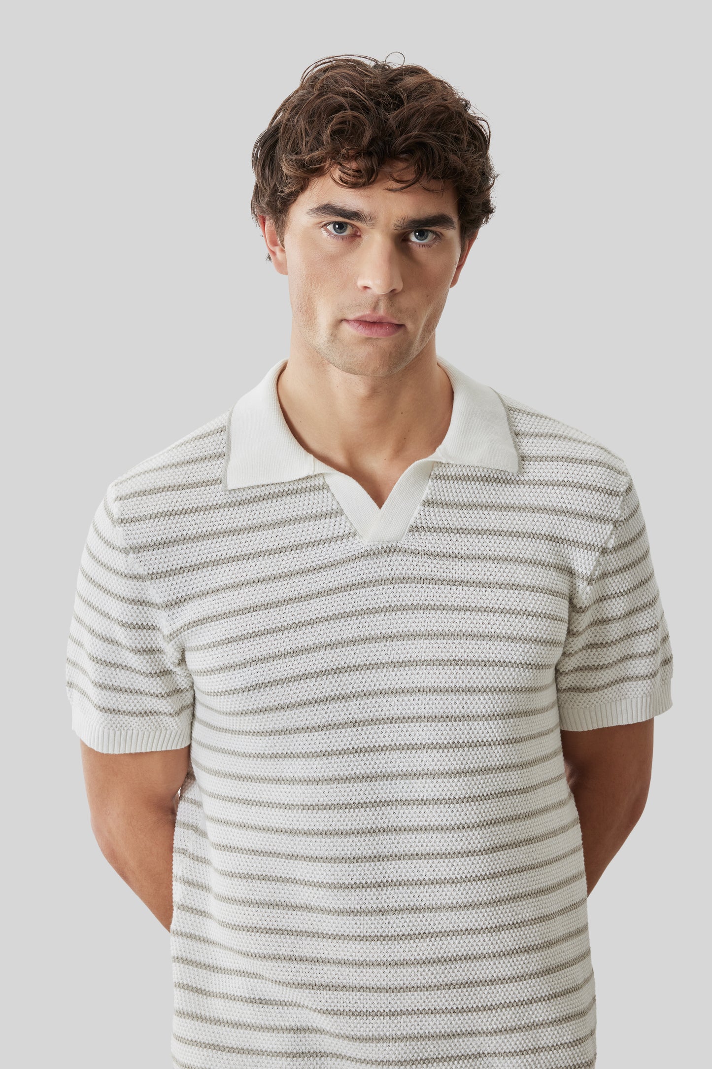 Man wearing cream and gray striped short-sleeve polo with open collar and white trim.