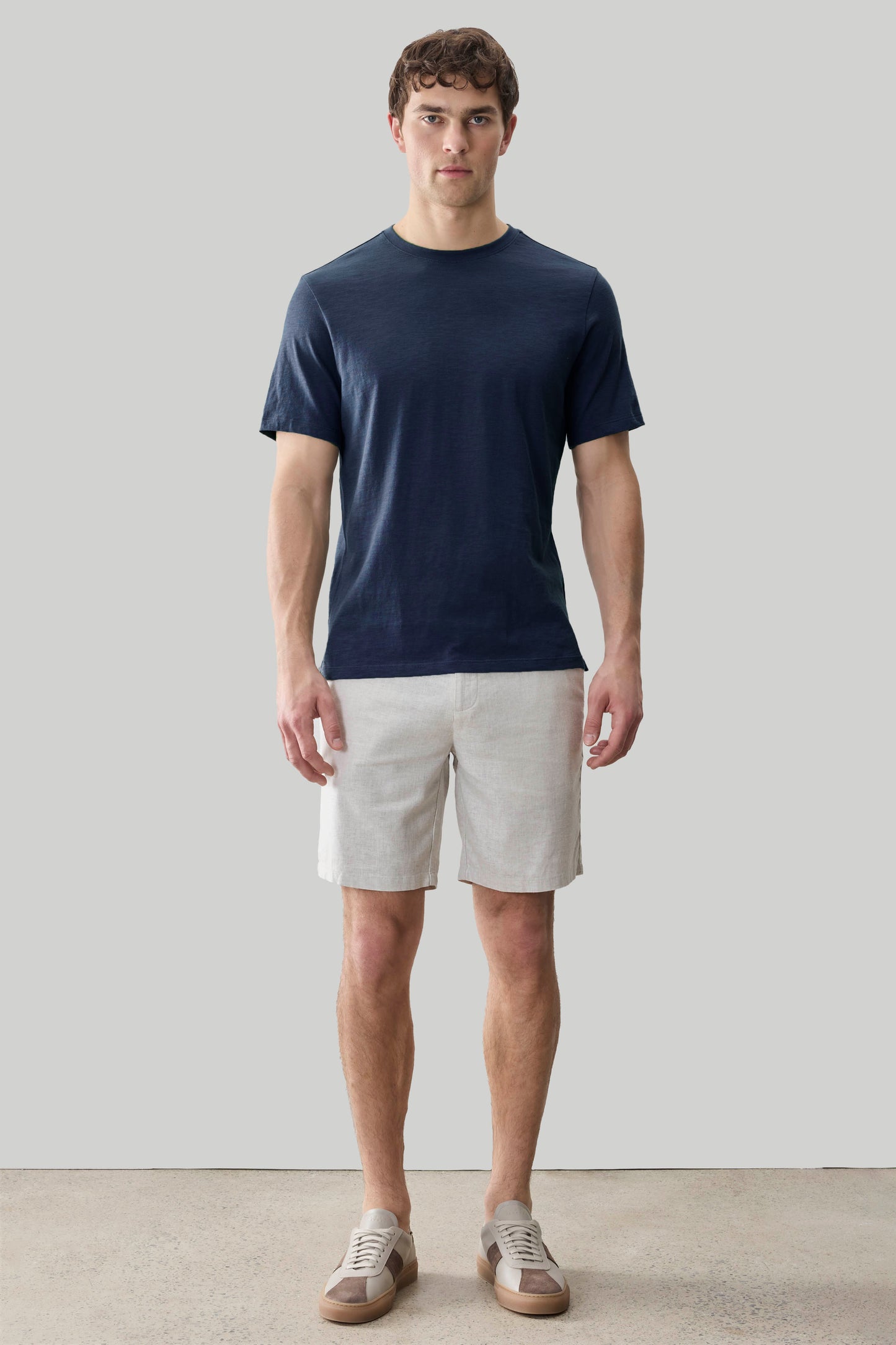 Man wearing dark navy short-sleeve crew neck tee with textured fabric and light gray shorts.