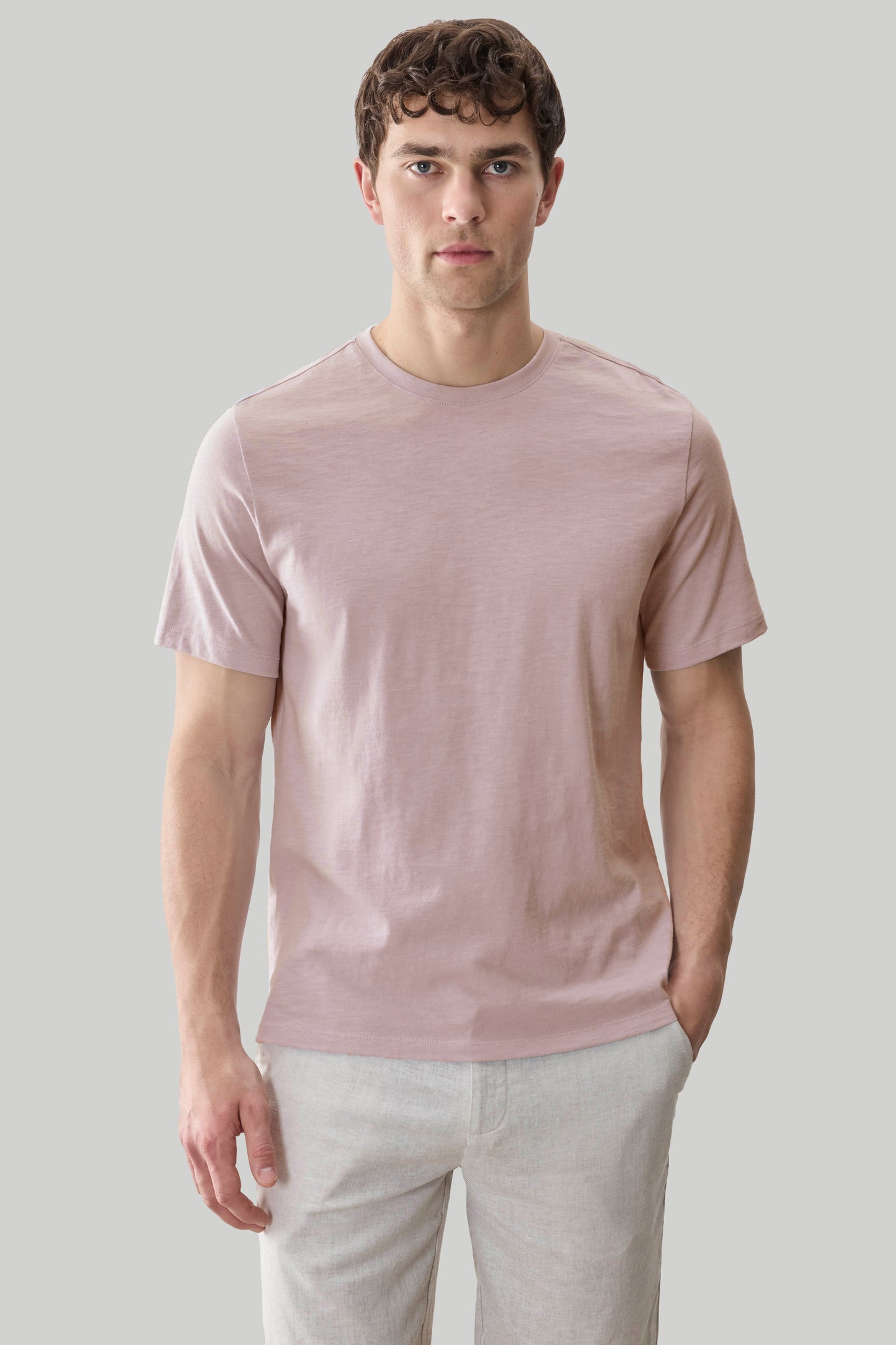 Man wearing a mauve short-sleeve t-shirt with a crew neckline and textured fabric, paired with light gray pants.