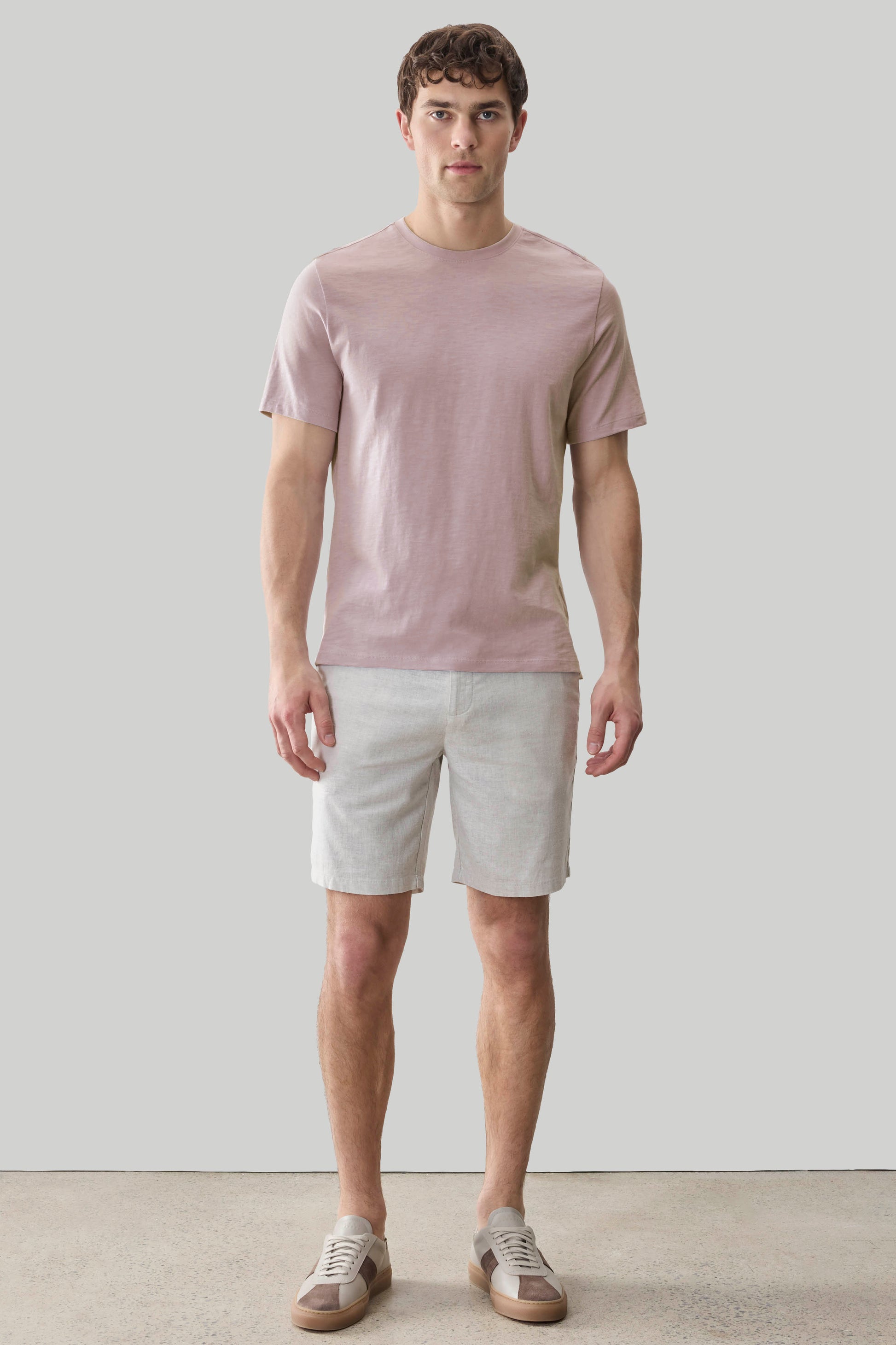 Man wearing dusty pink short-sleeve t-shirt and beige shorts with white sneakers.