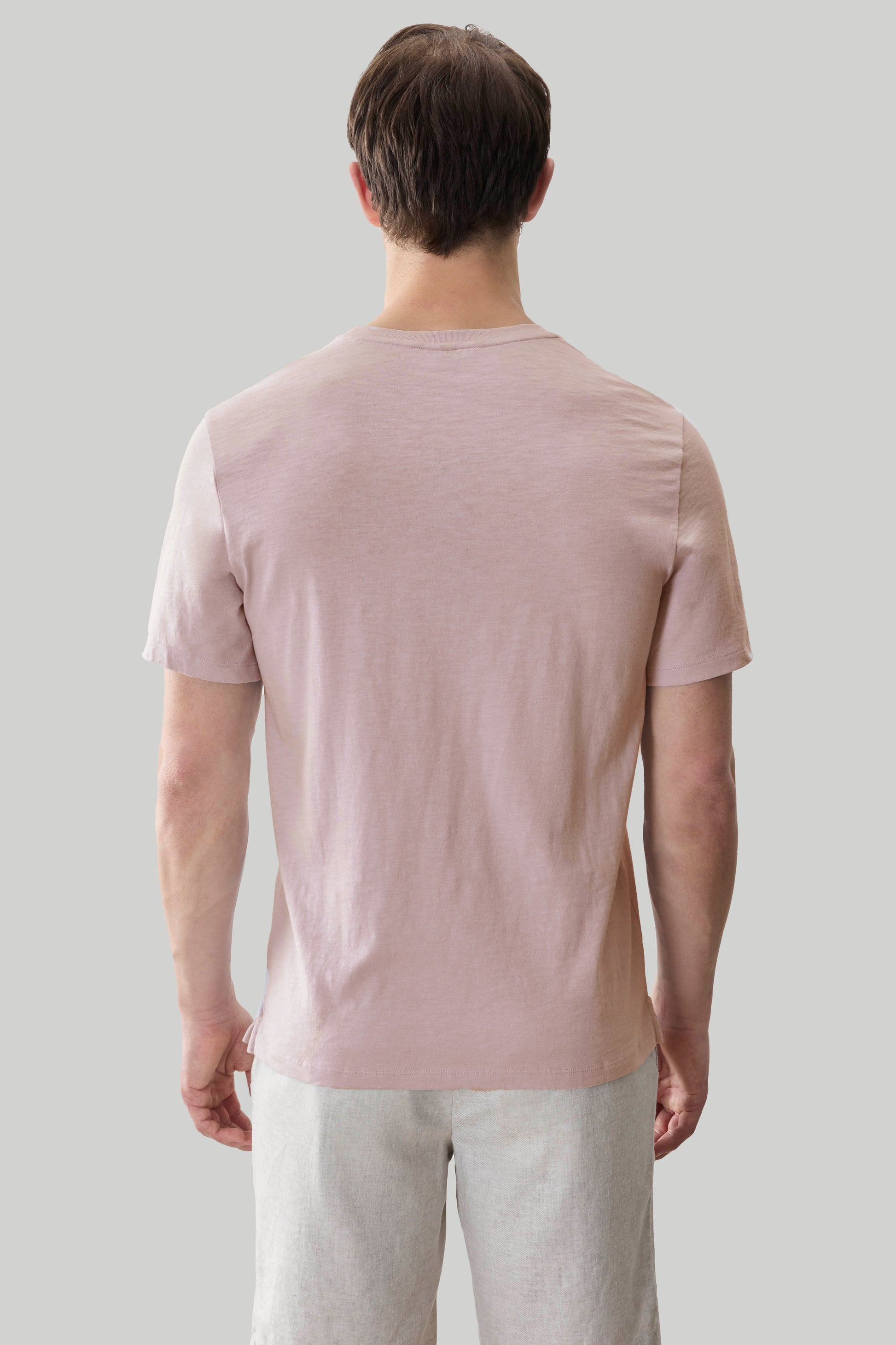 Man wearing a light pink short-sleeve t-shirt and light gray pants, shown from behind.