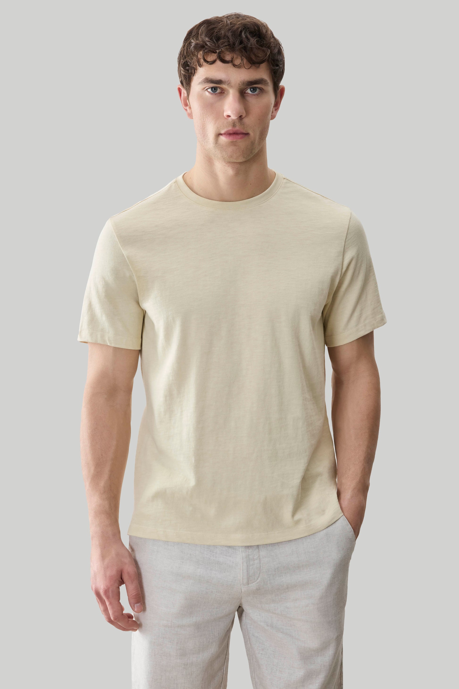 Cream-colored short sleeve t-shirt with crew neckline worn by a man with light pants.
