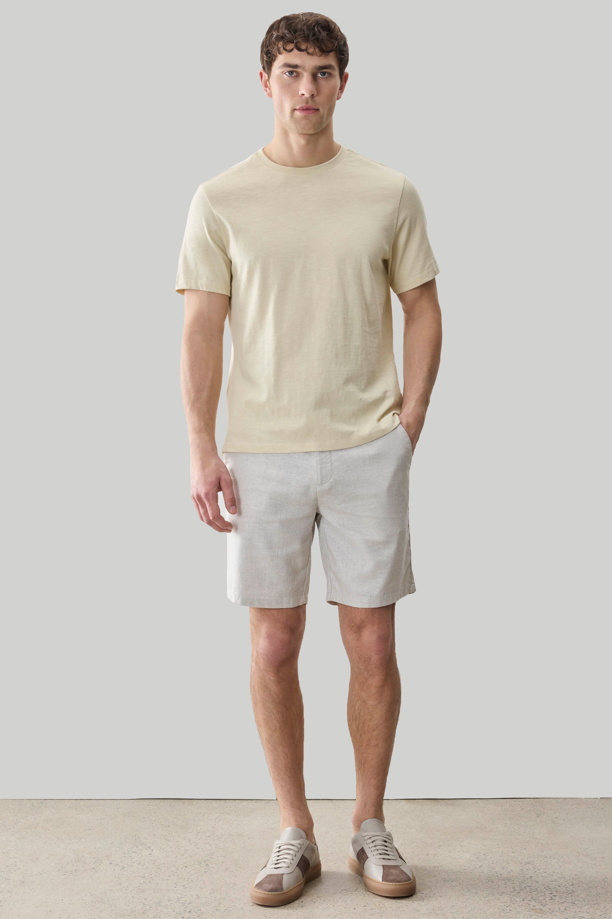 Man wearing cream short-sleeve t-shirt and light gray shorts with canvas sneakers.