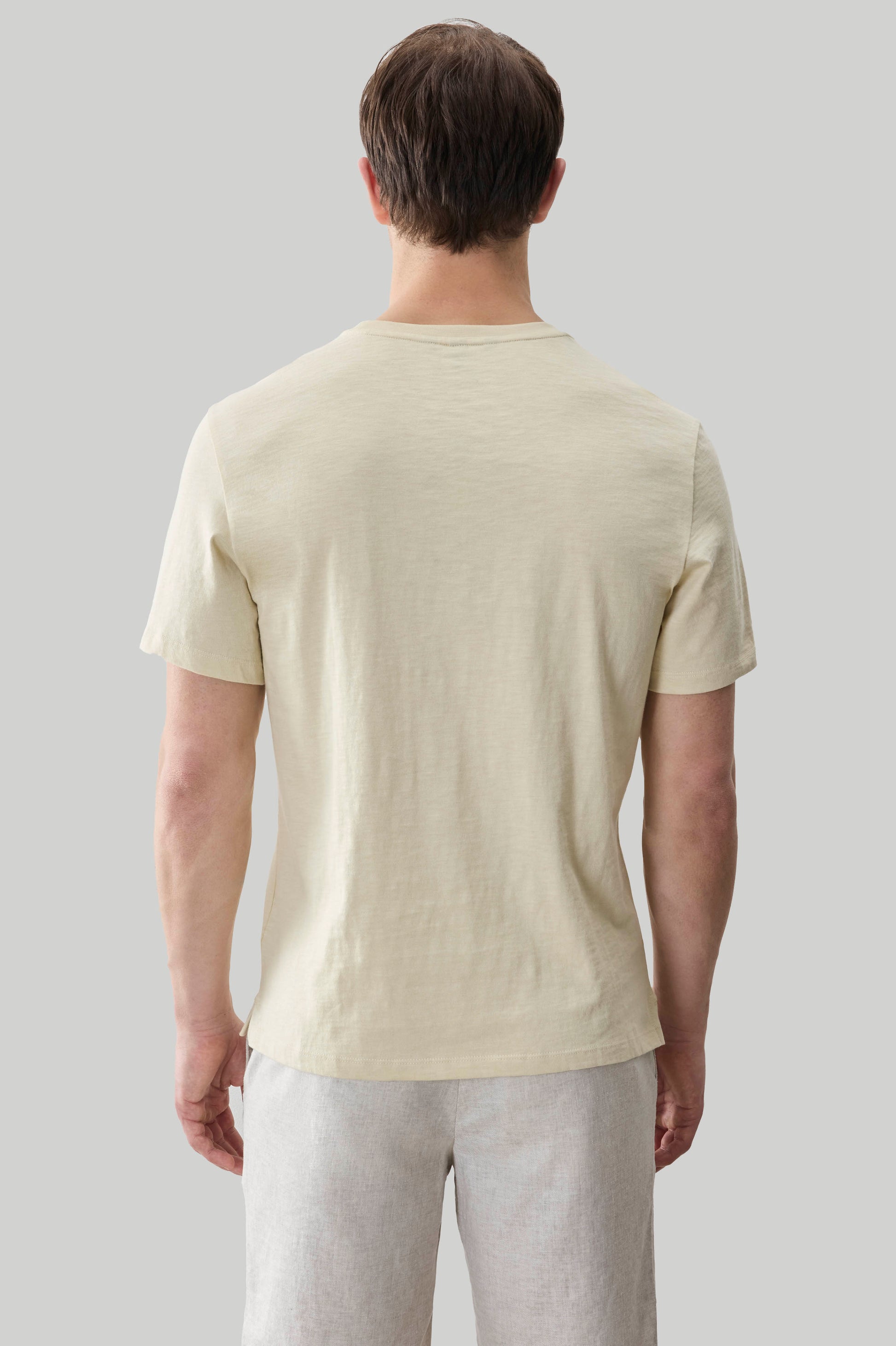 Man wearing a cream short-sleeve slub tee with light gray pants, shown from the back.