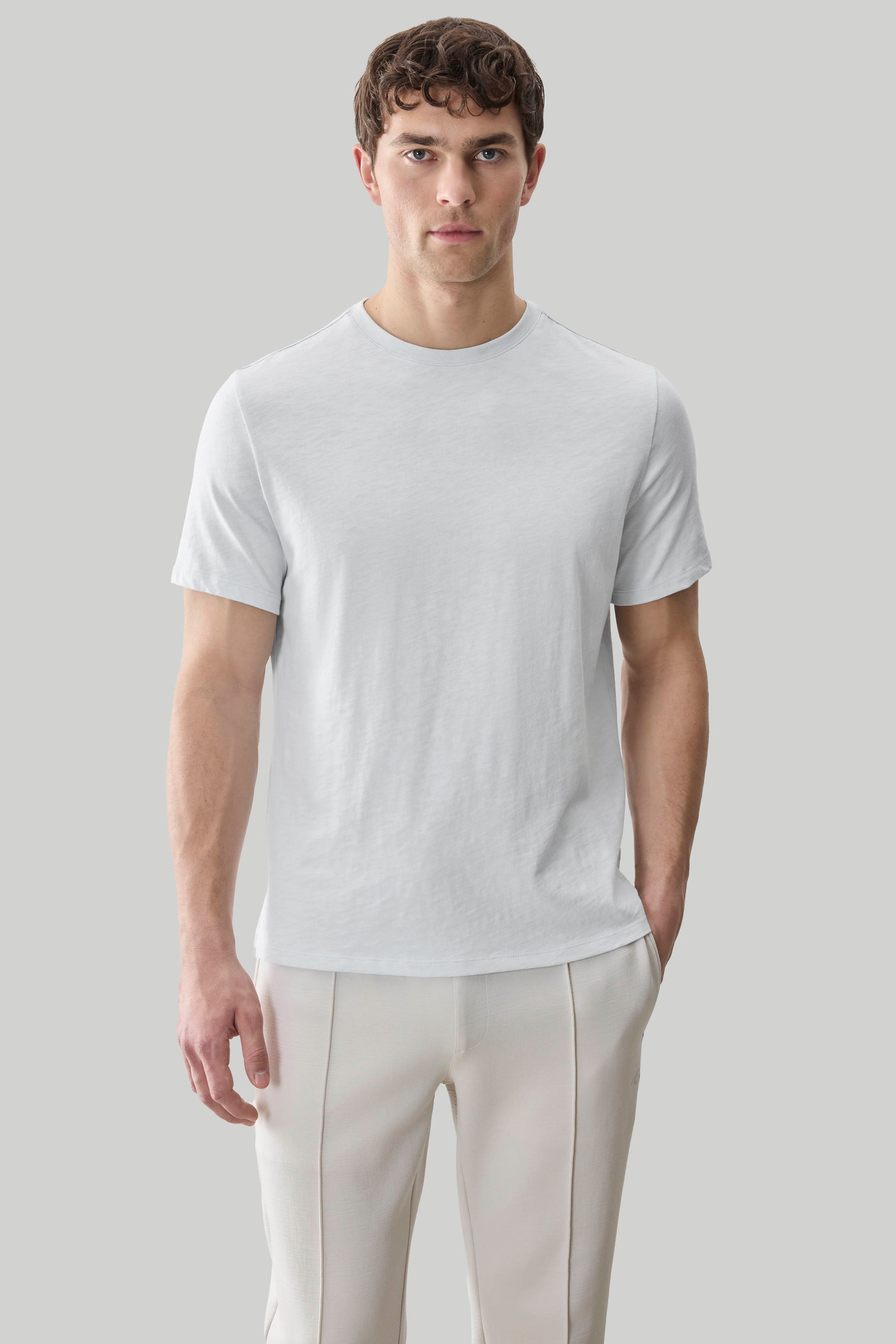Man wearing a light gray short-sleeve crew neck tee with textured fabric paired with cream-colored pants.