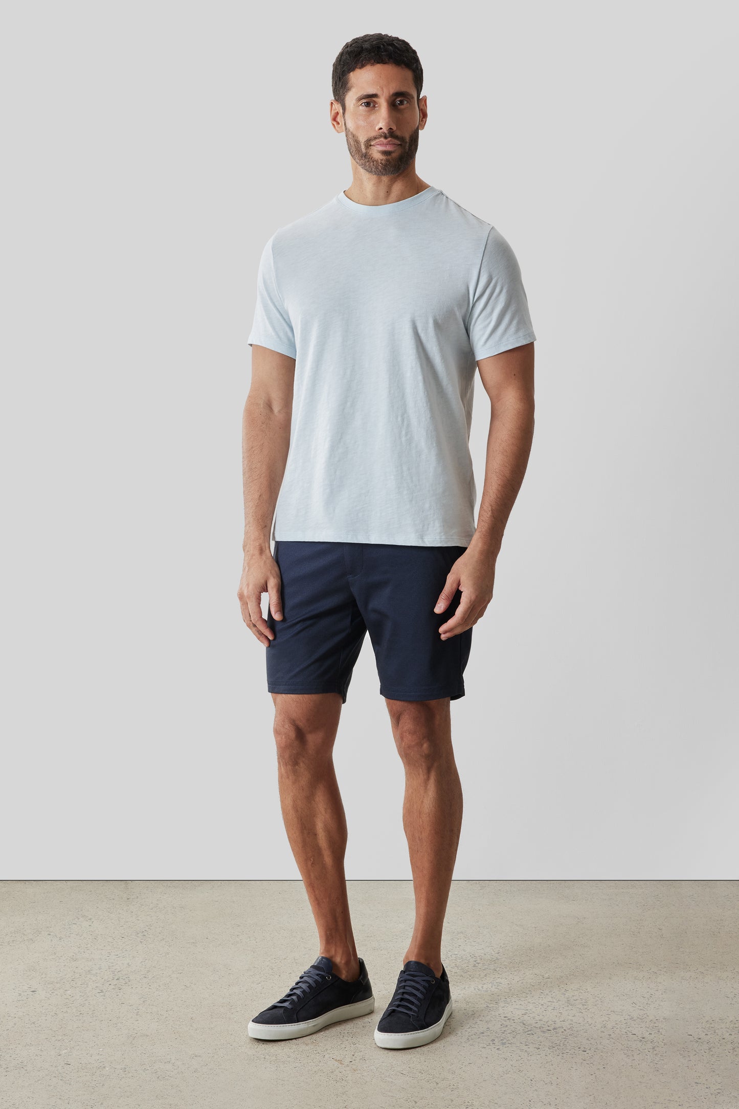 Man wearing light blue short-sleeve crew neck tee with dark navy shorts and black sneakers.