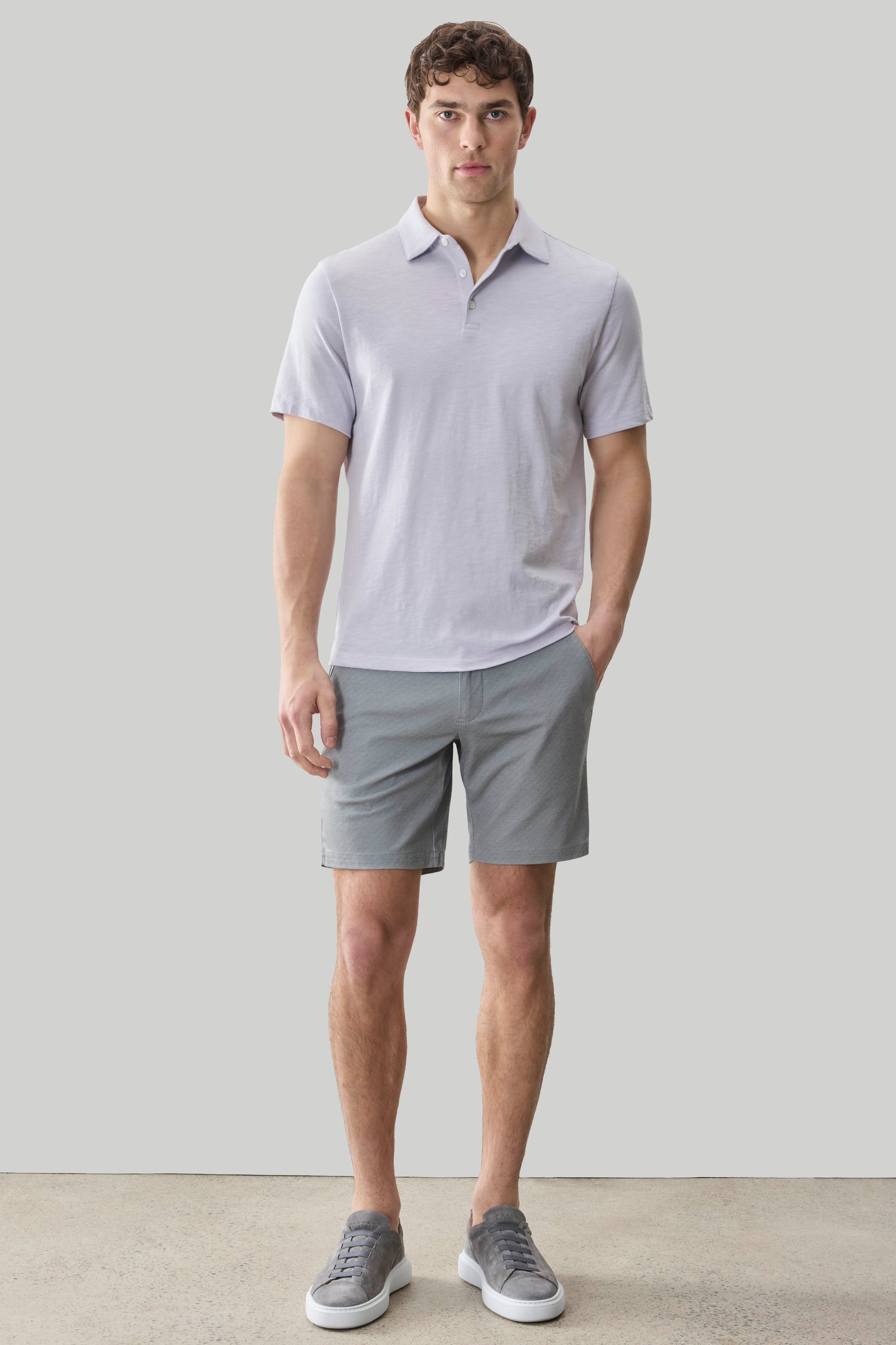 Man wearing light purple short-sleeve polo shirt with collar and button placket, paired with gray shorts and gray sneakers.