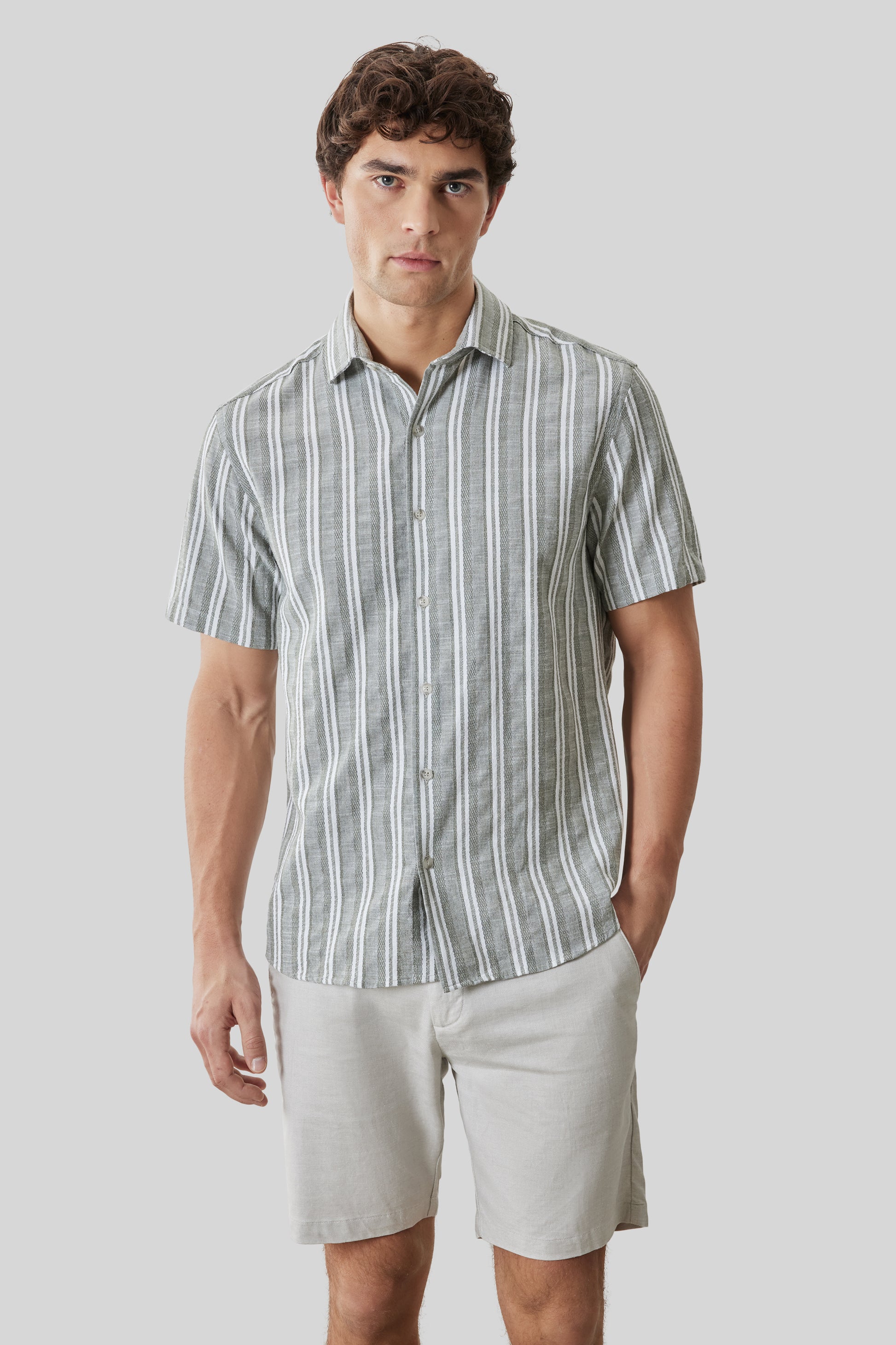 Man wearing gray and white striped short-sleeve button-up shirt with cream shorts.
