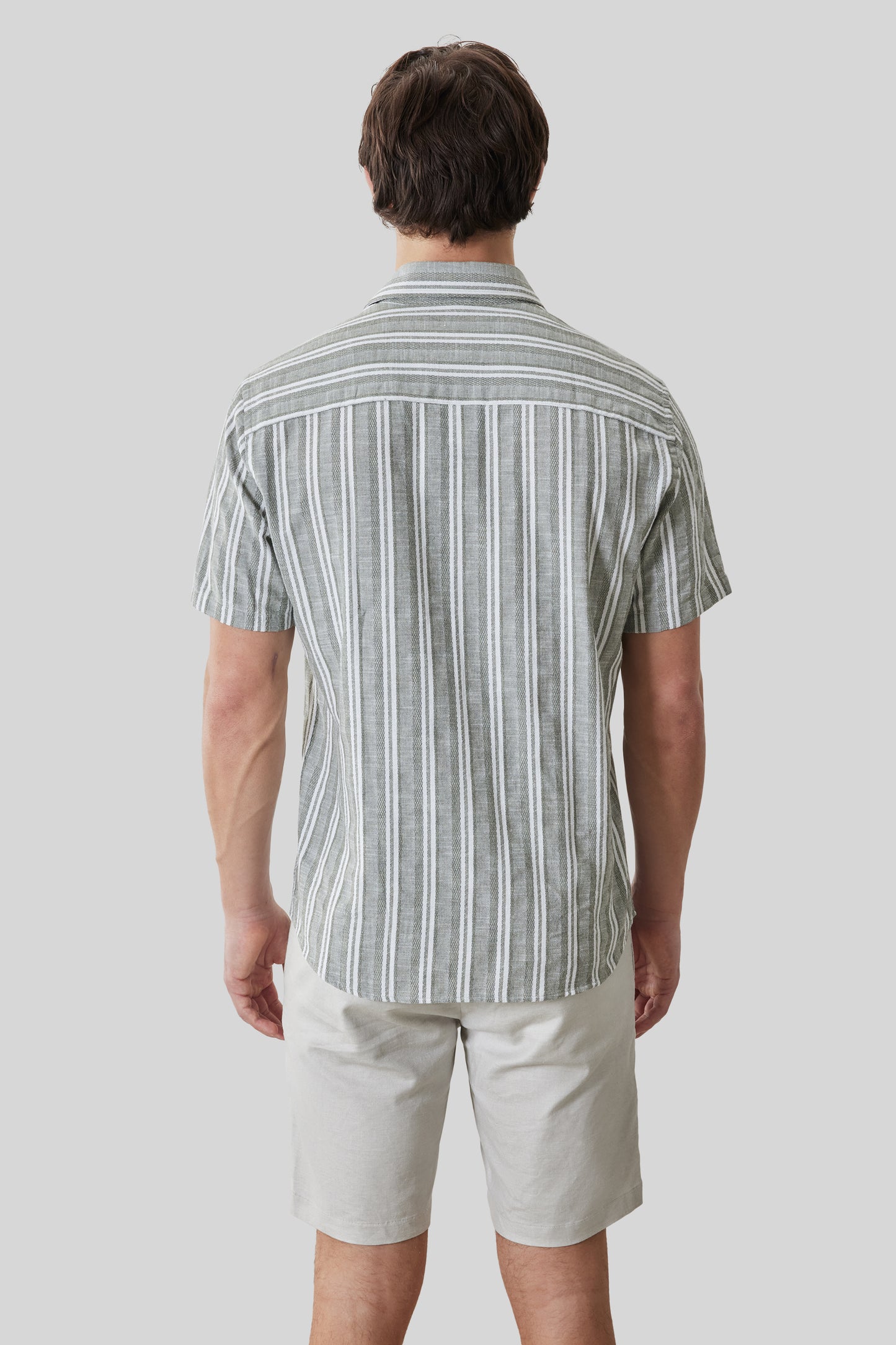 Man wearing gray and white striped short-sleeve shirt with white shorts, shown from behind.
