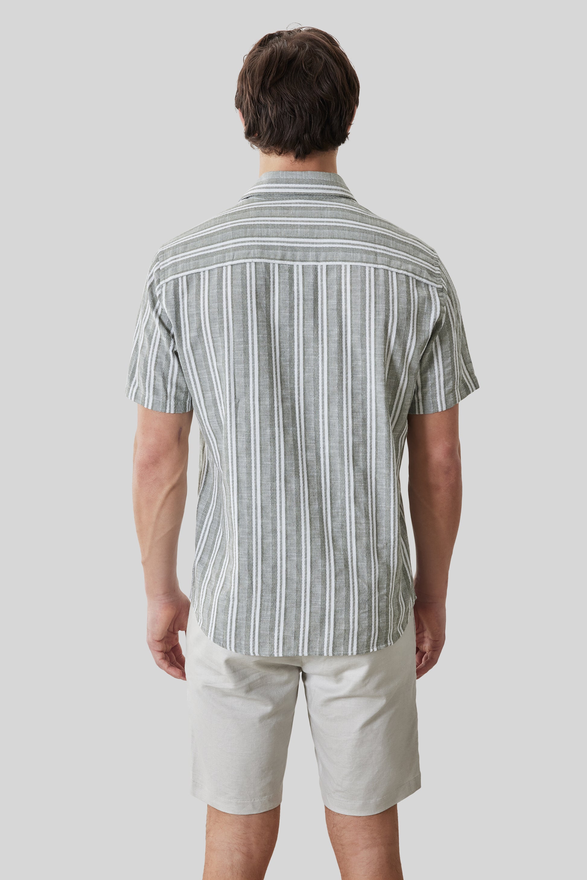 Man wearing gray and white striped short-sleeve shirt with white shorts, shown from behind.