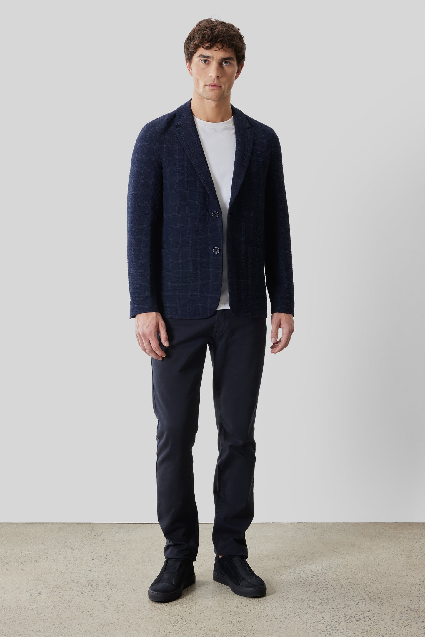 Navy check sportcoat with notch lapels and button closure worn over white t-shirt with matching navy trousers.
