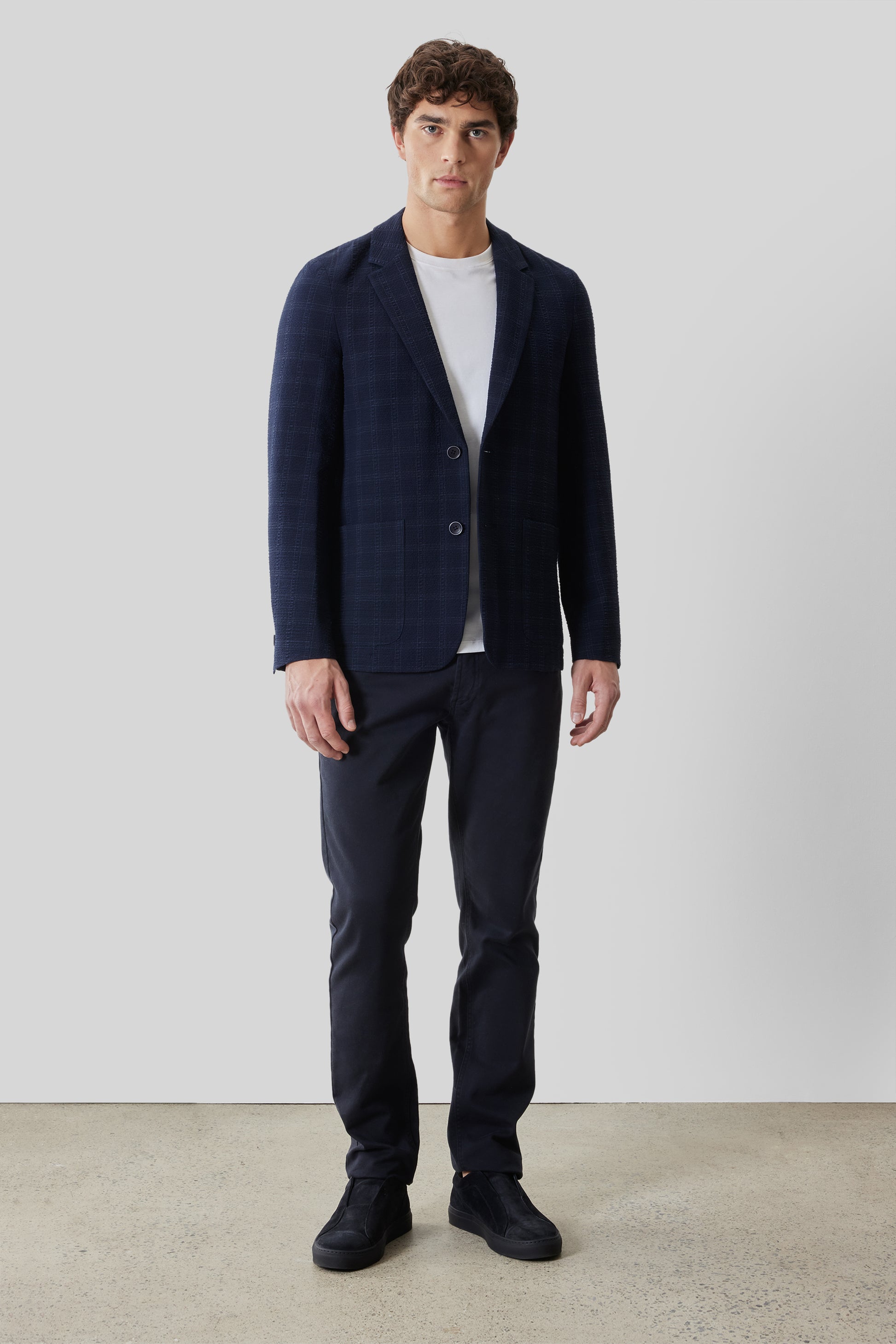Navy check sportcoat with notch lapels and button closure worn over white t-shirt with matching navy trousers.