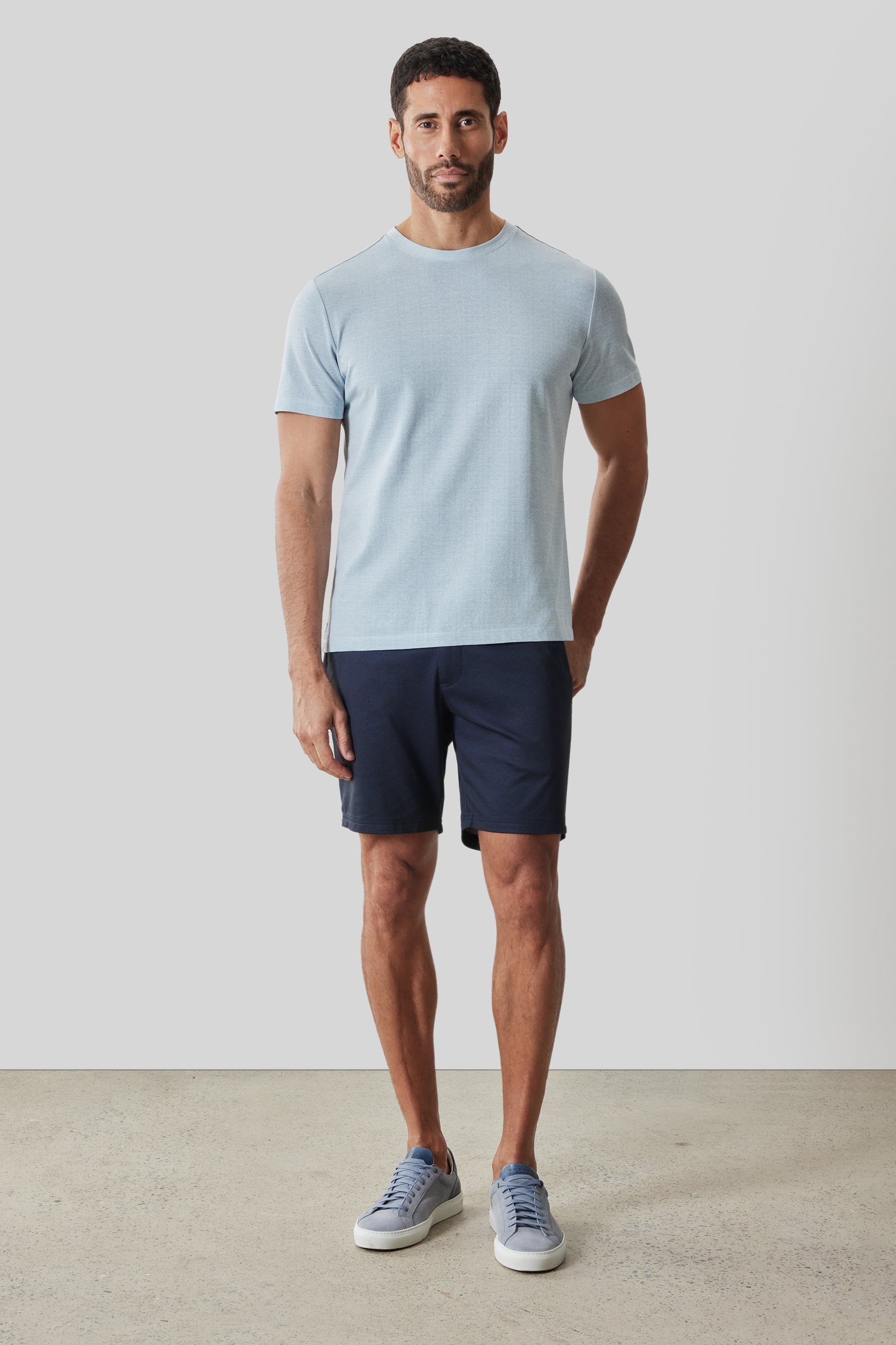 Man wearing light blue short-sleeve t-shirt and dark navy shorts with blue sneakers.