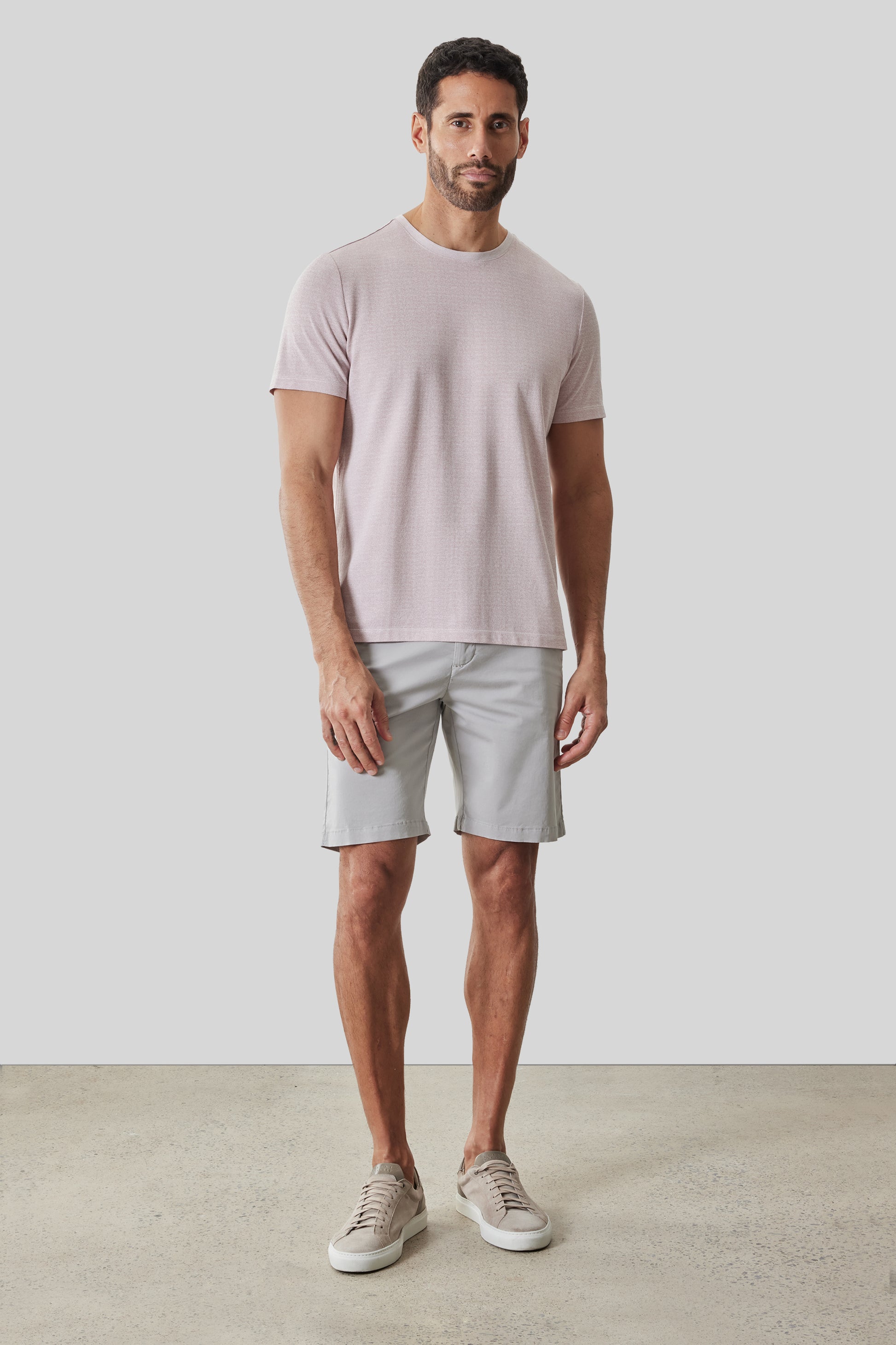 Man wearing pale pink short-sleeve crew neck t-shirt with gray shorts and canvas sneakers.