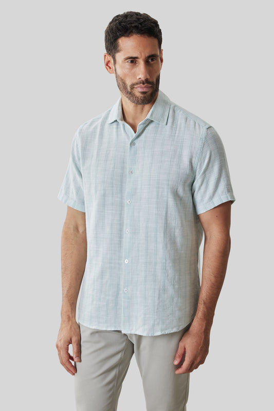 Light blue plaid short sleeve button-up shirt with white buttons, displayed on a model wearing beige pants.