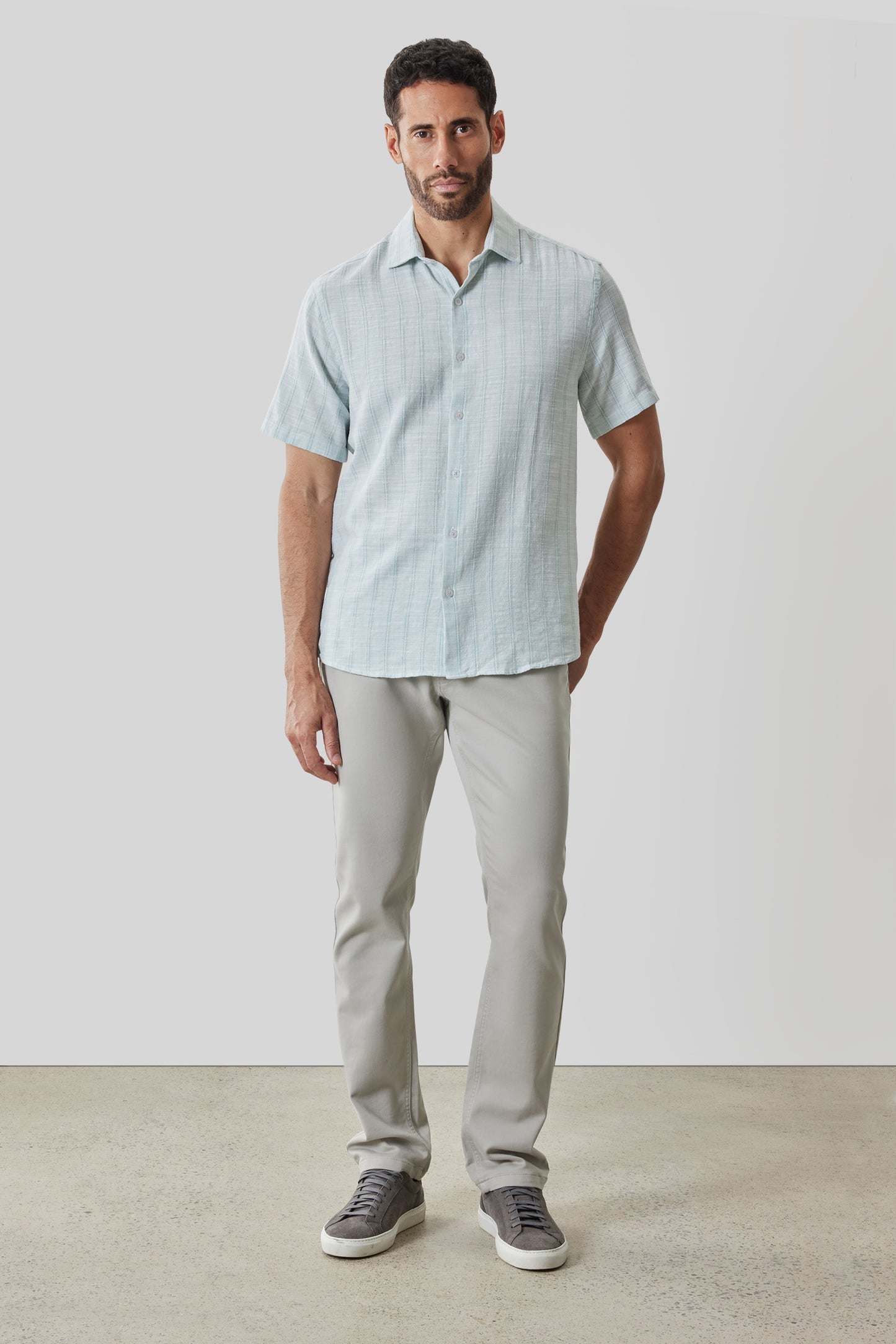Man wearing light blue short-sleeve button-up shirt with grid pattern and beige pants.