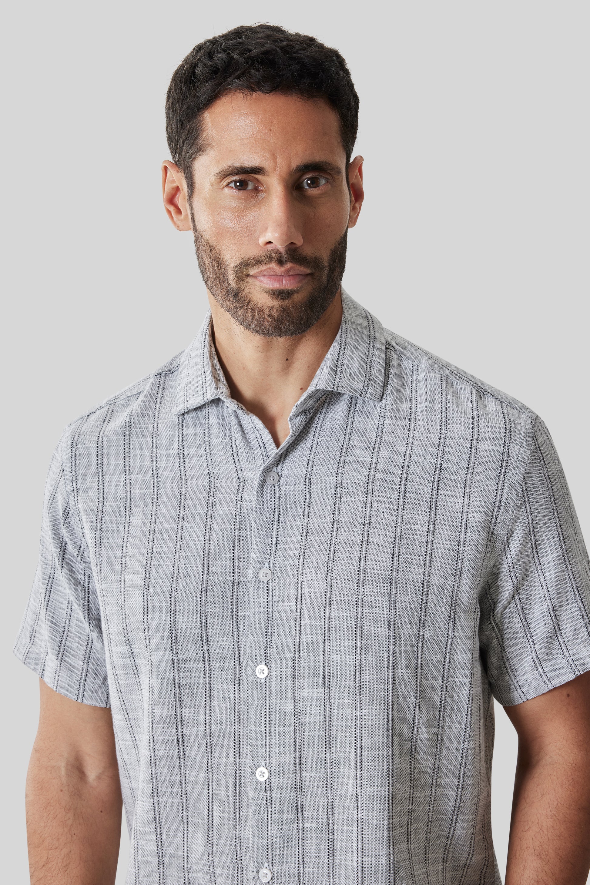 Light gray short sleeve button-up shirt with vertical pinstripe pattern worn by man against neutral background.