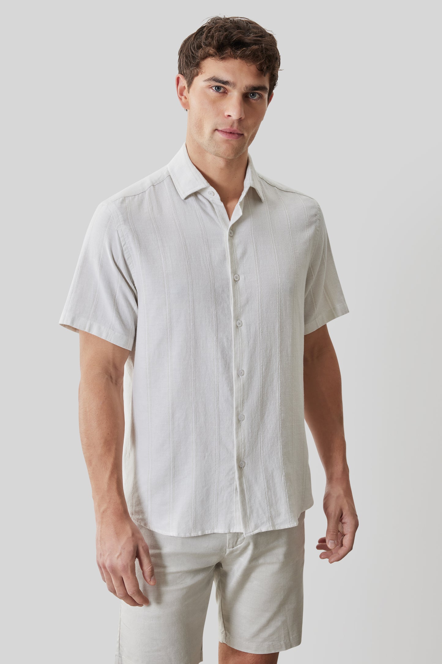 White linen short-sleeve button-up shirt with spread collar on model wearing light pants.