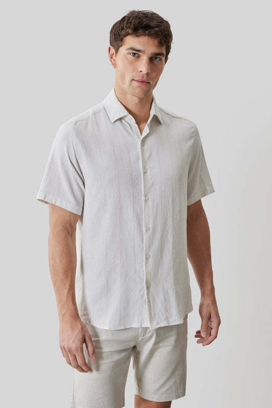 White linen short-sleeve button-up shirt with spread collar on model wearing light pants.