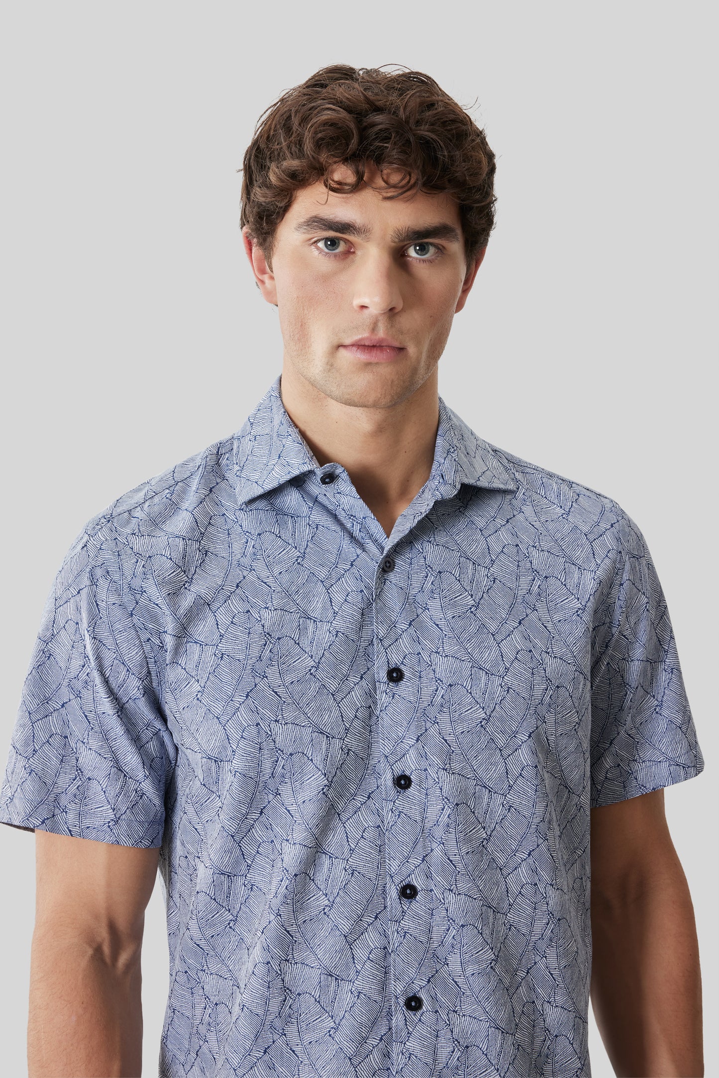 Man wearing light blue short-sleeve button-up shirt with abstract line pattern and dark buttons.