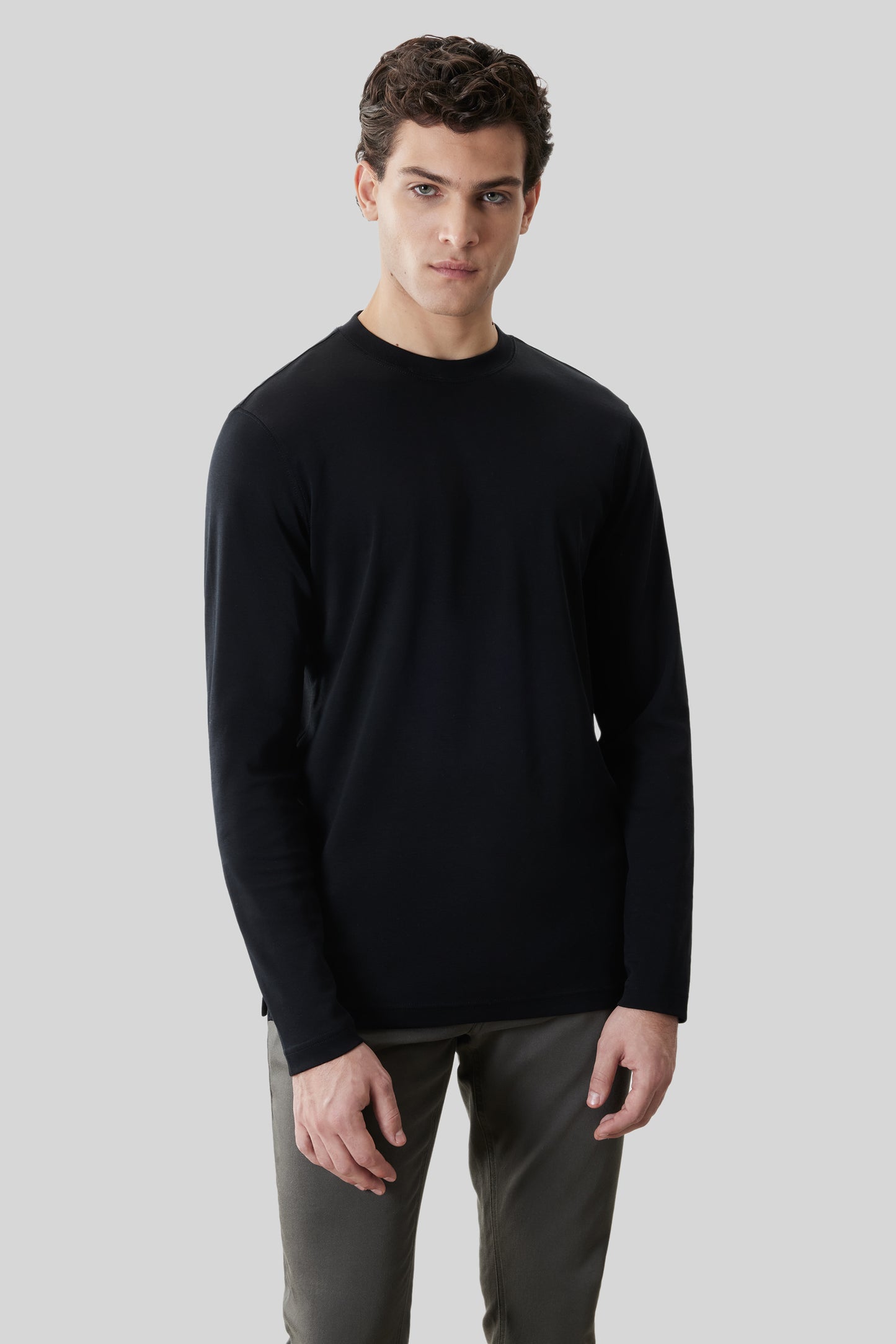 Man wearing black long-sleeve crew neck shirt with olive green pants against neutral background.