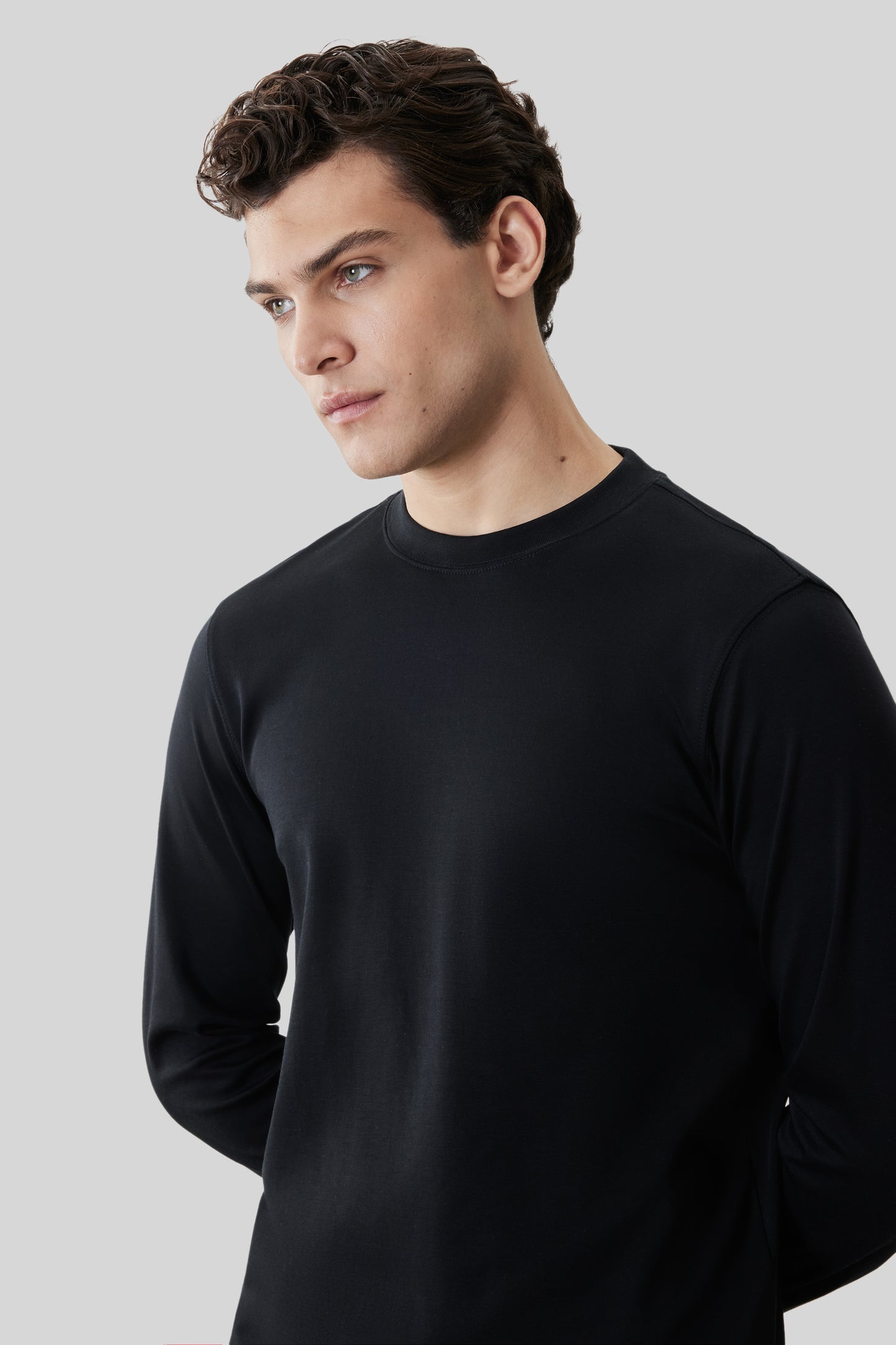 Man wearing black crew neck long-sleeve shirt against neutral background.