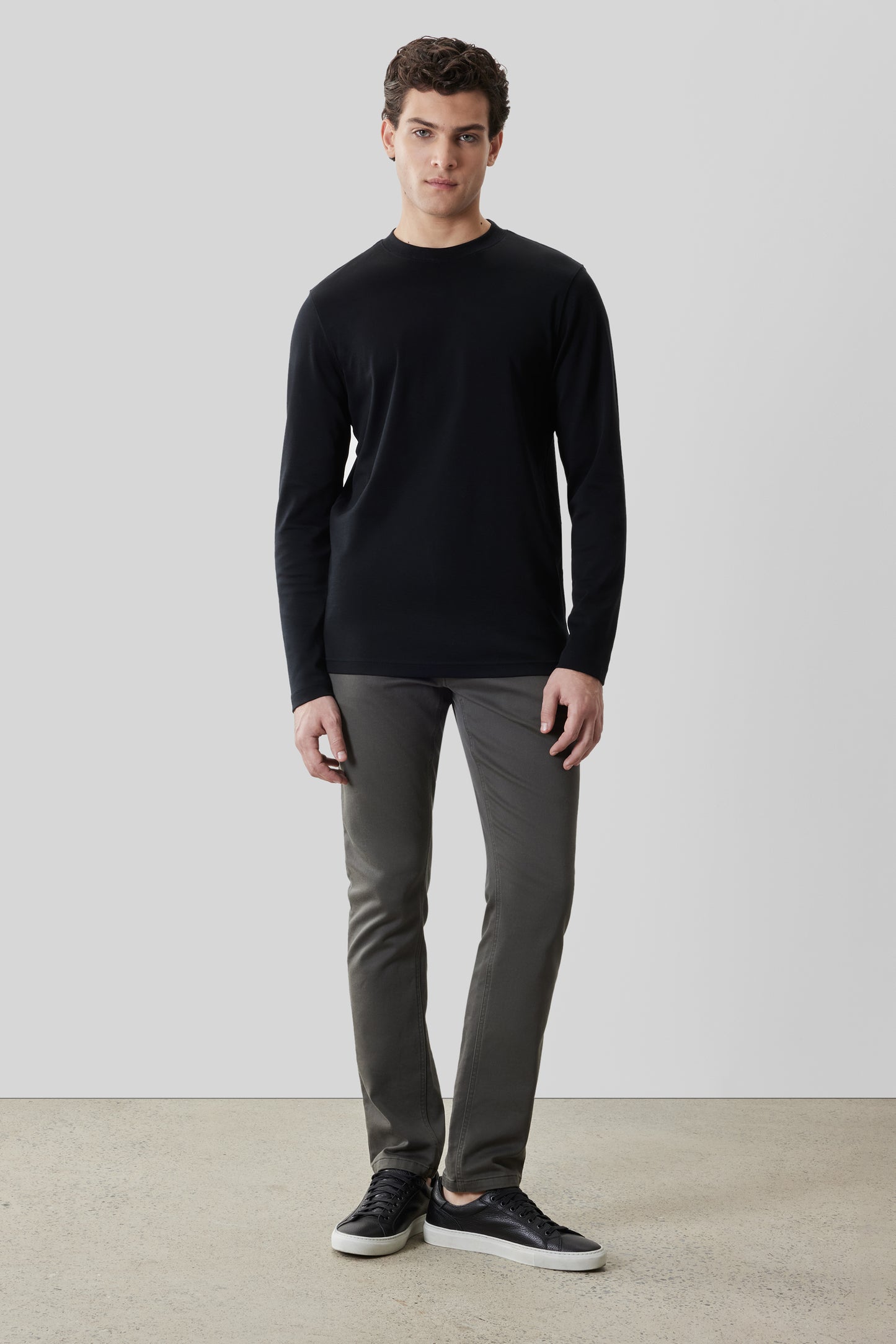 Man wearing black crew neck long-sleeve shirt with gray pants and black sneakers.