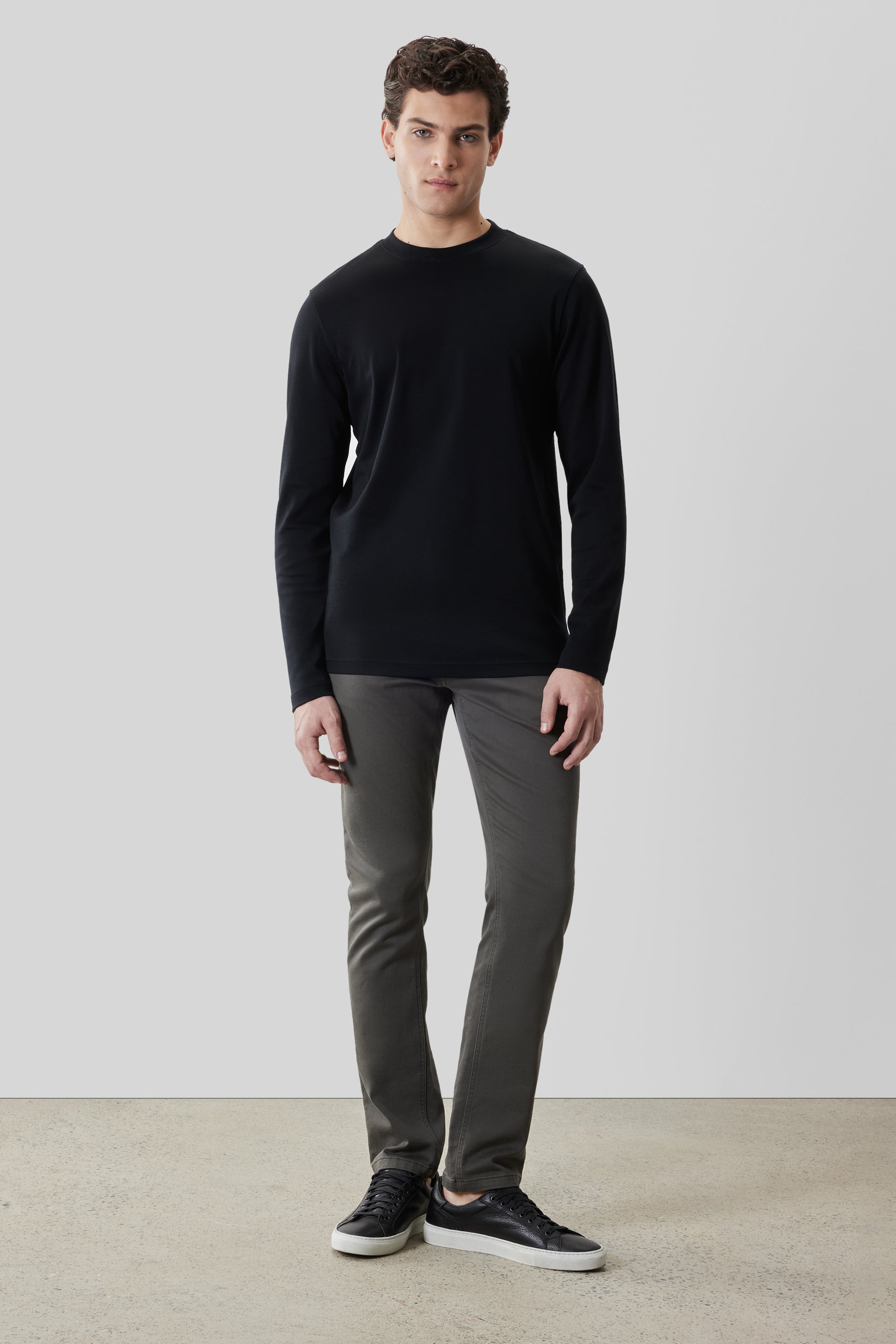 Man wearing black crew neck long-sleeve shirt with gray pants and black sneakers.
