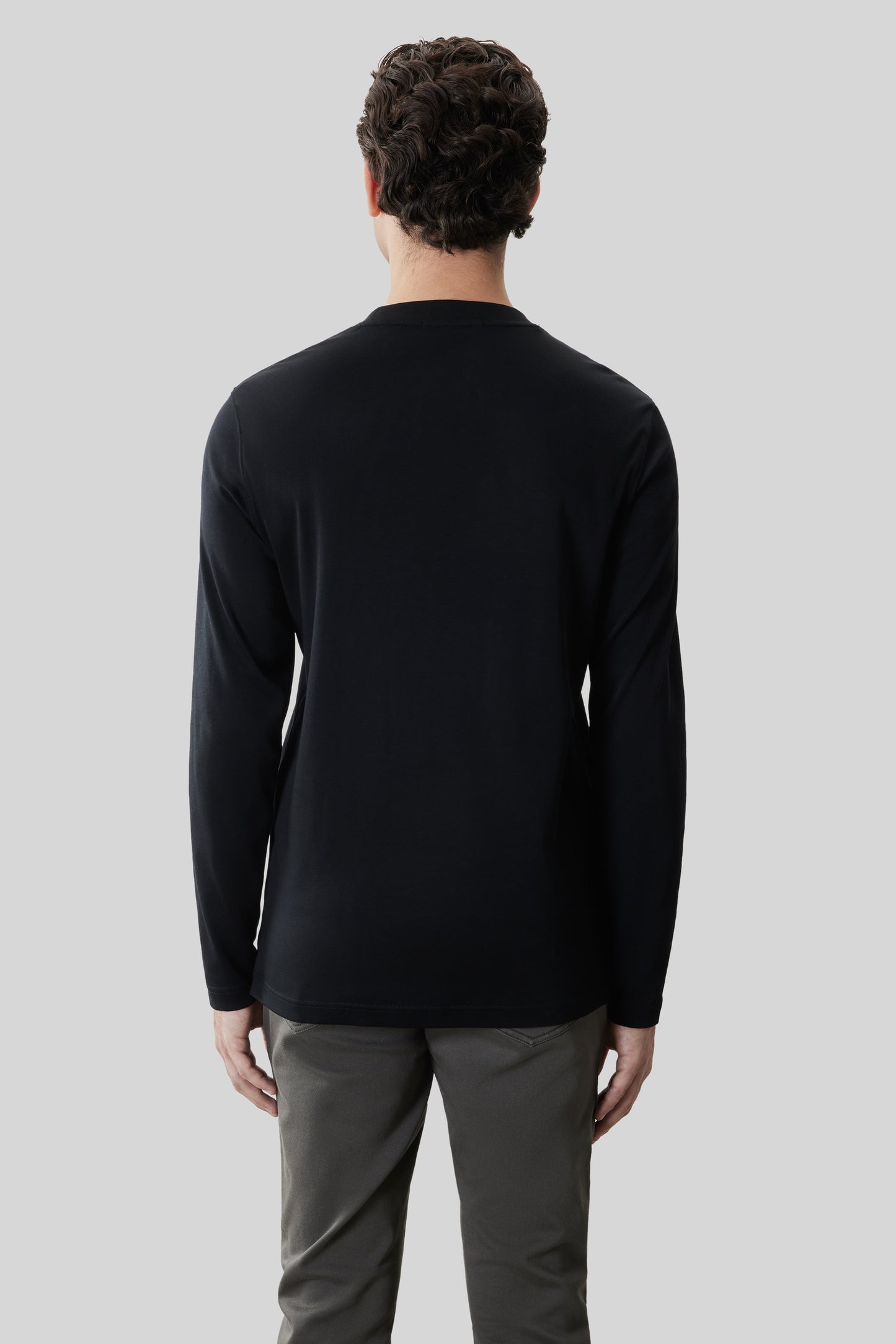 Man wearing black long-sleeve crew neck shirt and gray pants, shown from back view.
