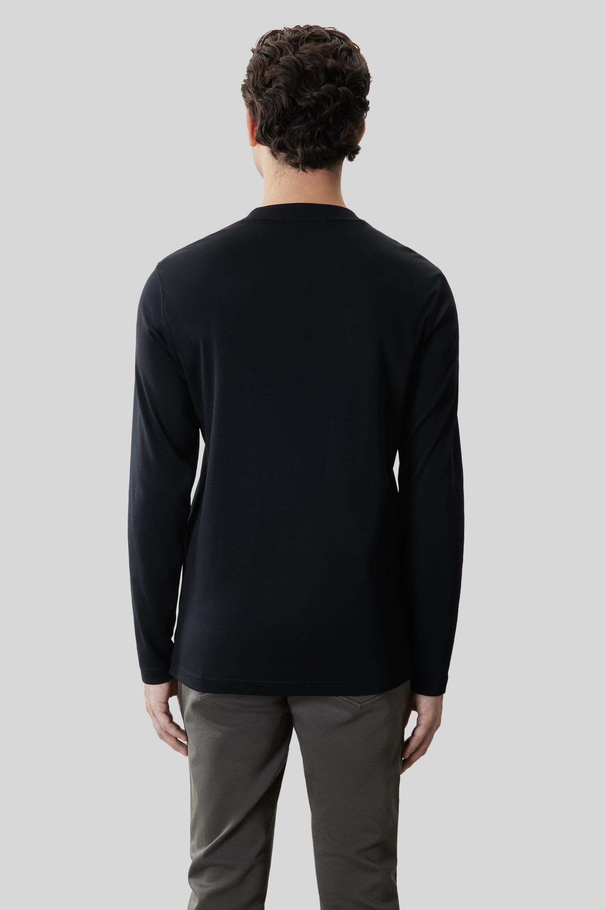 Man wearing black long-sleeve crew neck shirt and gray pants, shown from back view.