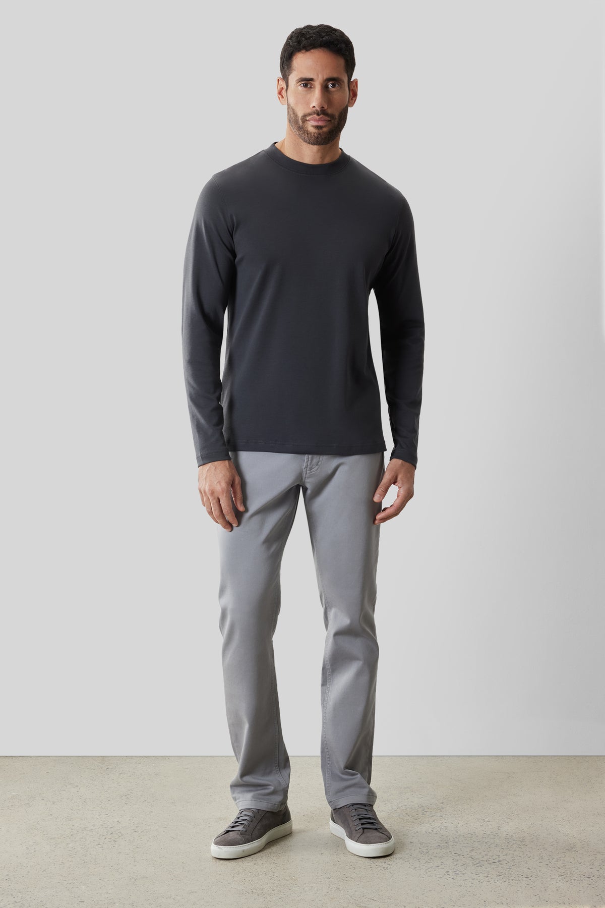 Man wearing black long-sleeve crew neck shirt with gray pants and dark sneakers.