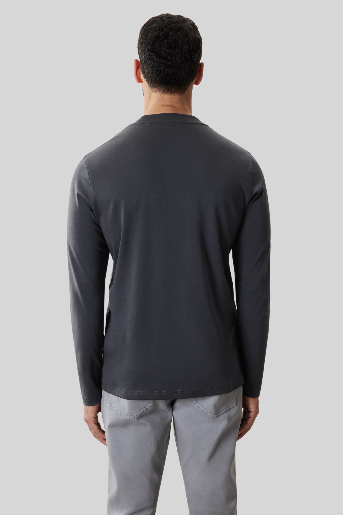 Man wearing dark navy long-sleeve crew neck shirt paired with light gray pants, shown from back view.