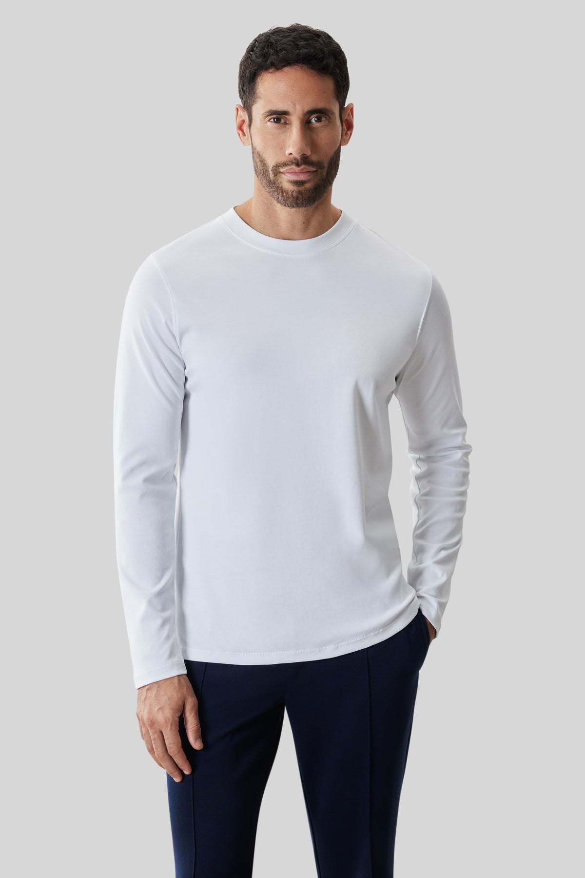 Man wearing white long-sleeve crew neck shirt with dark navy pants.