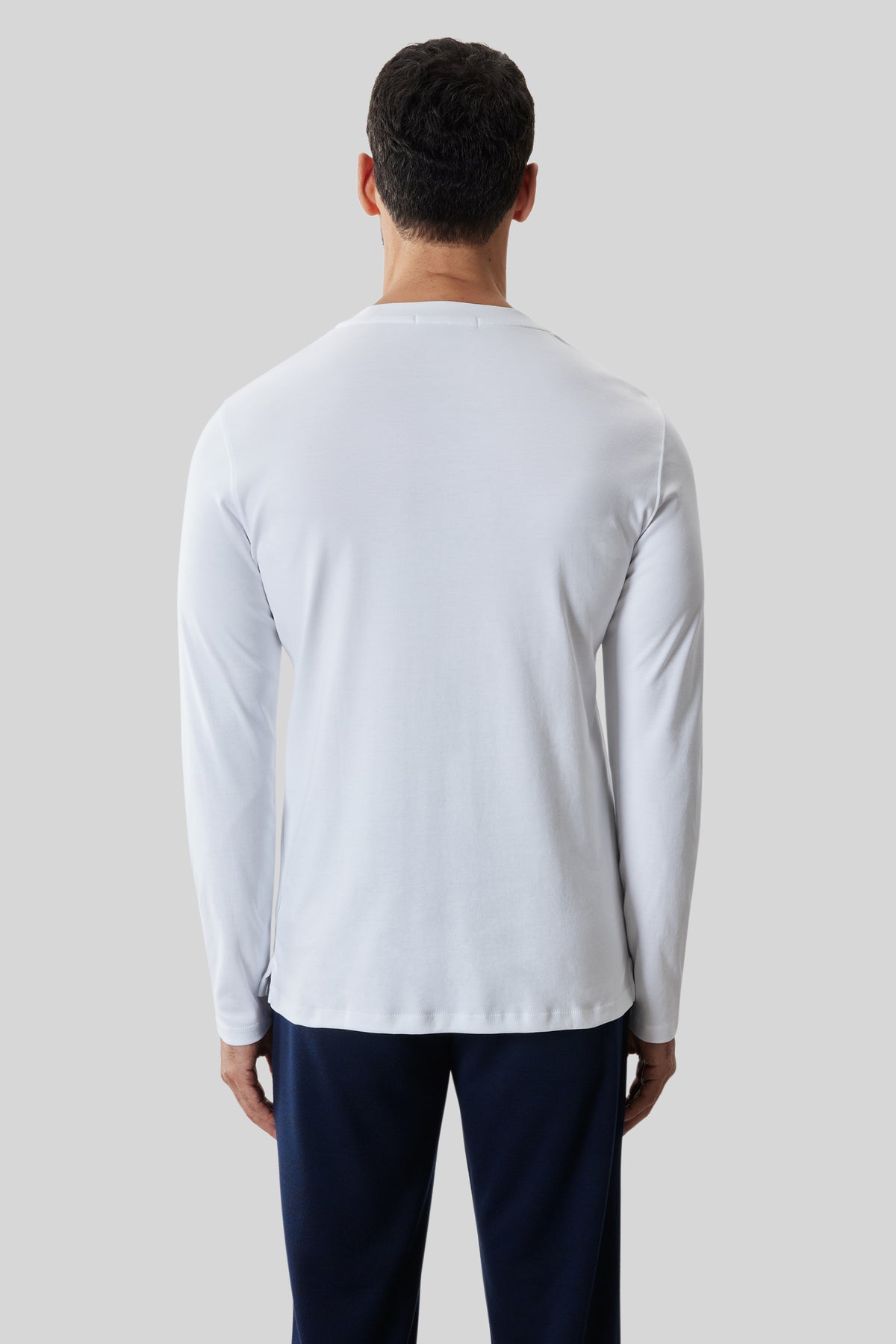 Man wearing white long-sleeve crew neck shirt and dark navy pants, back view.