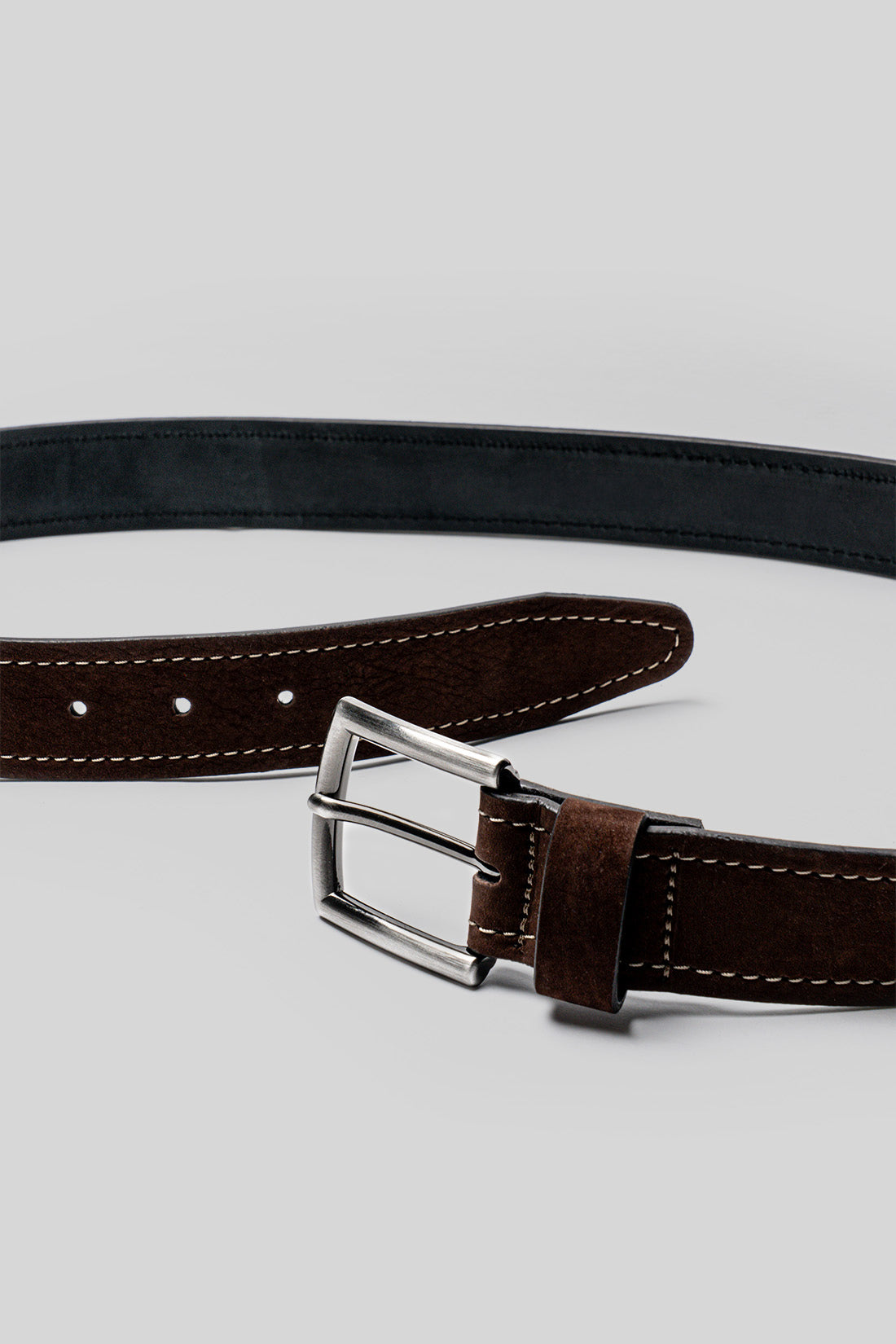 Brown and black leather belts with white stitching and metal buckles displayed overlapped against a gray background.