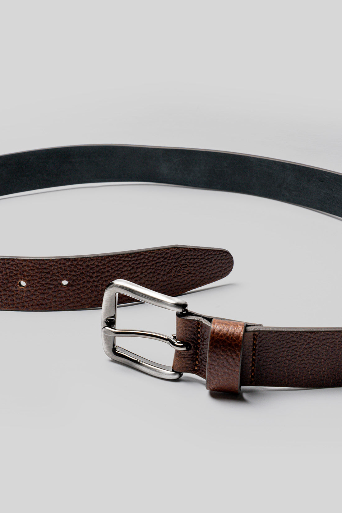 Brown leather belt with textured finish and silver buckle, shown with black belt coiled above.