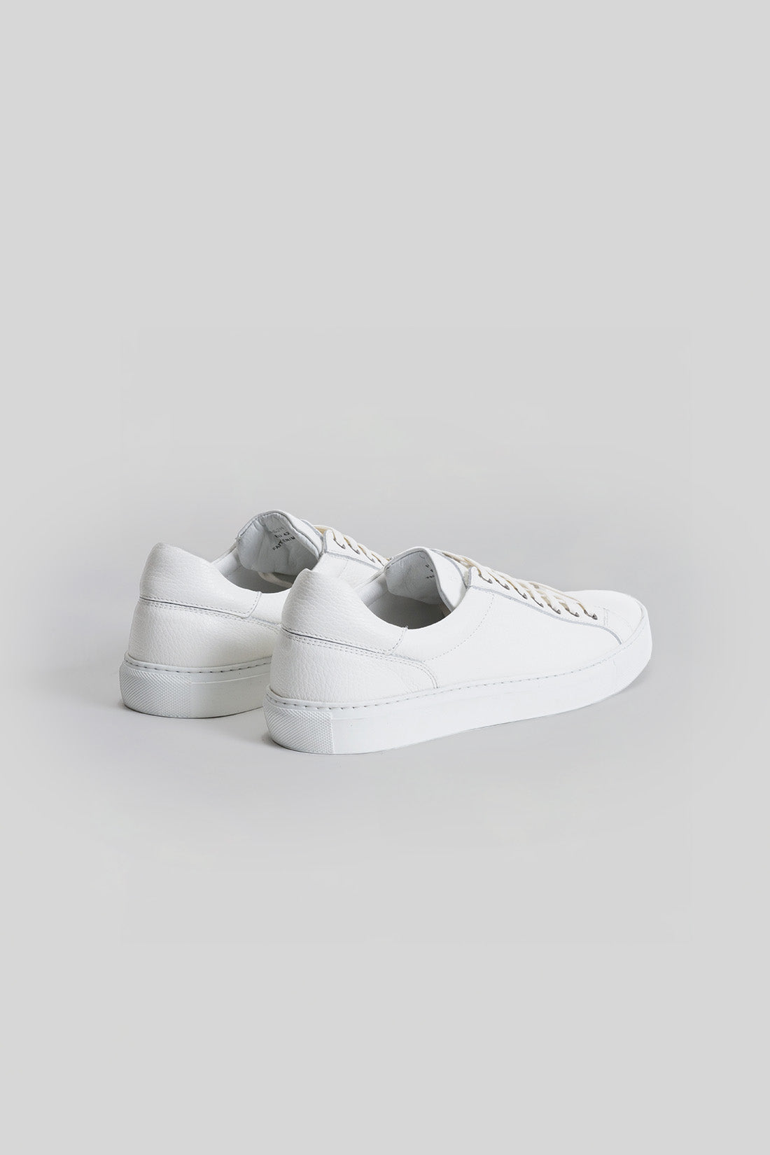 White leather low-top sneaker with lace-up closure shown from rear three-quarter angle.