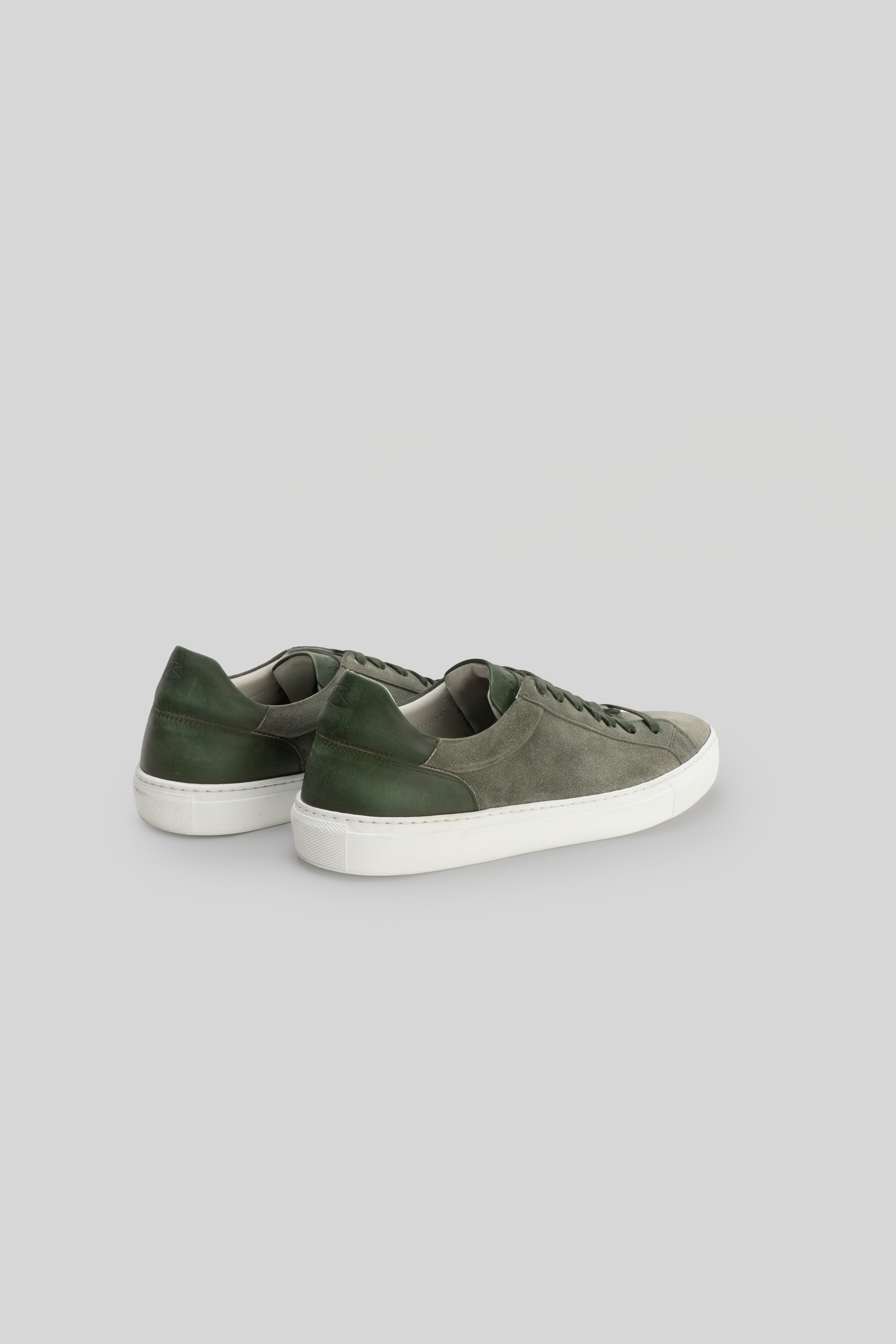 Pair of sneakers with gray suede upper and dark green heel counter, white rubber sole, shown from rear three-quarter view.