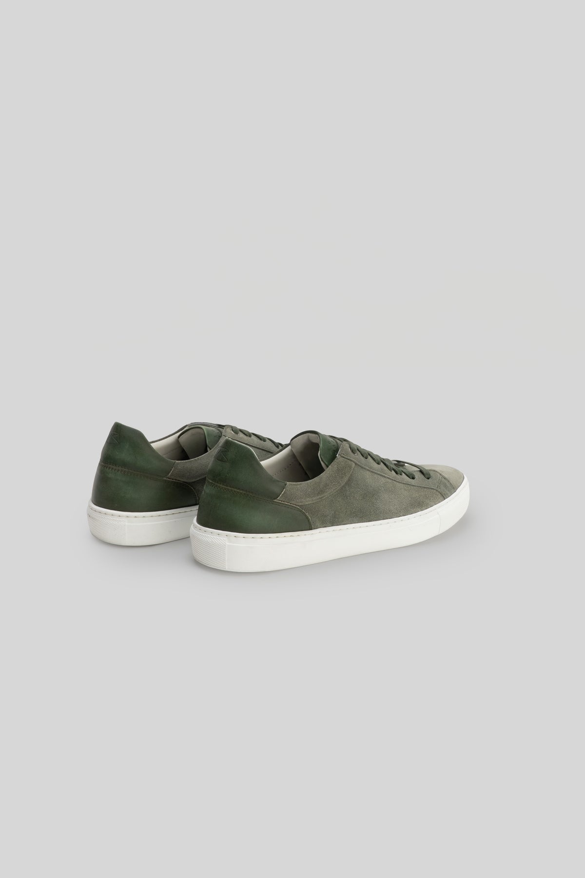 Pair of sneakers with gray suede upper and dark green heel counter, white rubber sole, shown from rear three-quarter view.