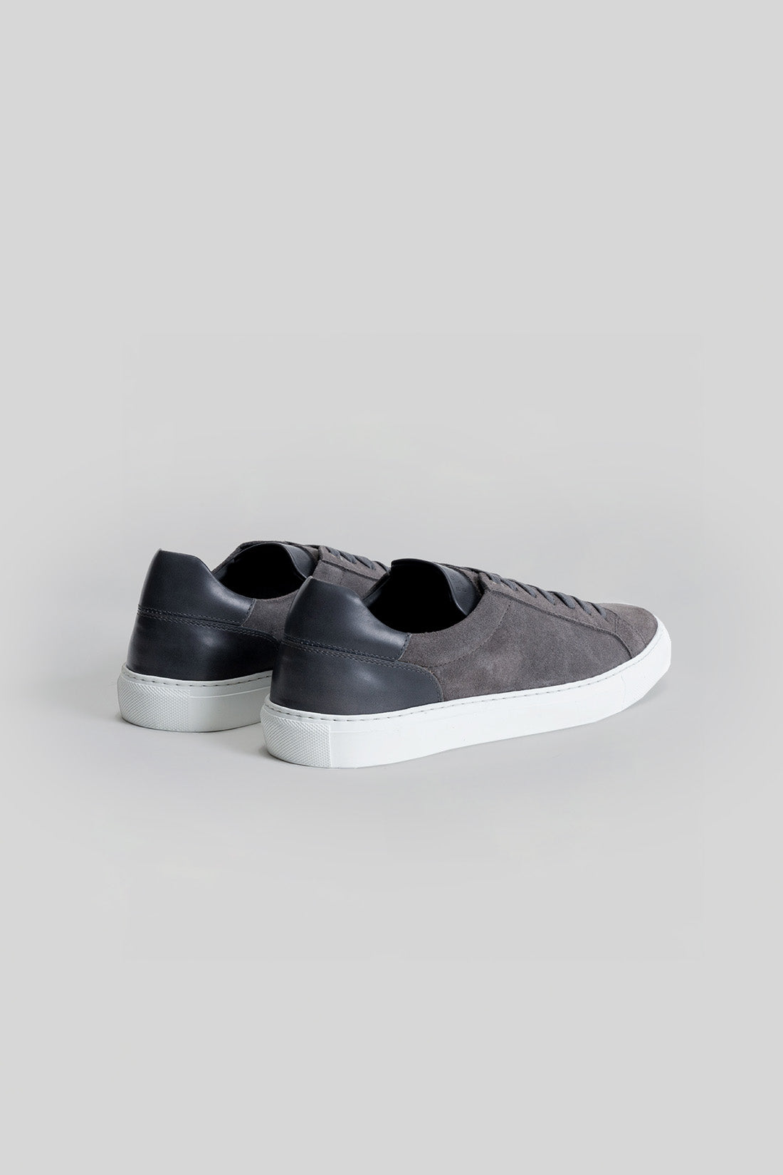 Gray suede and black leather sneaker with white sole, shown from rear three-quarter view.